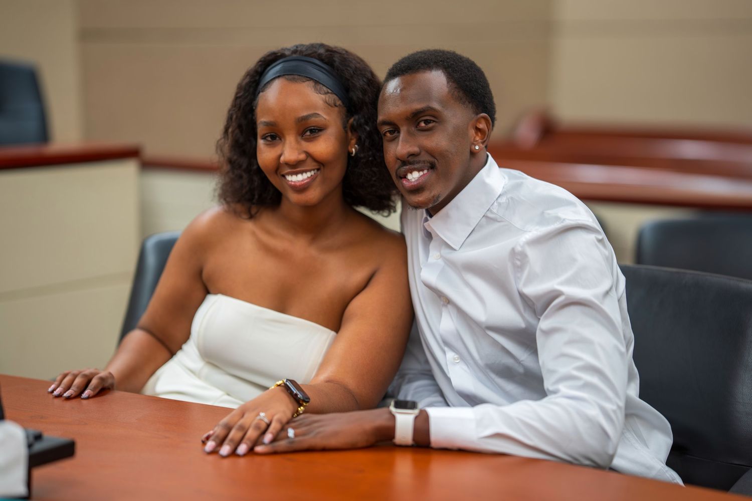 A happy newlywed couple in white attire smiles together at a courthouse table.