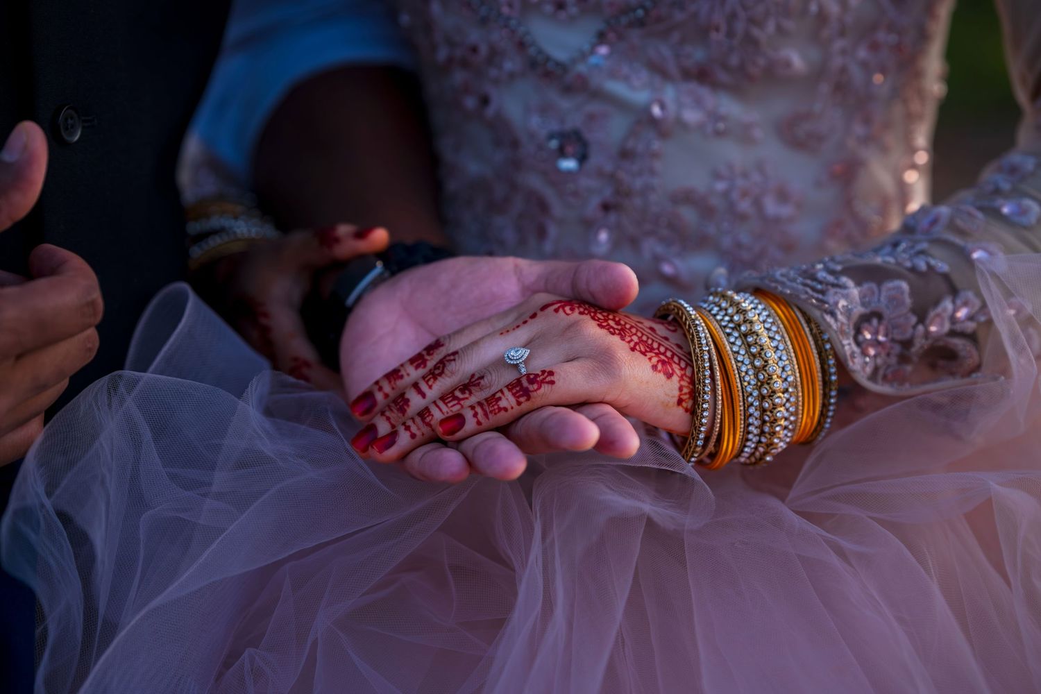 Close-up of bride's hands adorned with henna tattoo, gold bangles, and diamond ring on wedding dress.