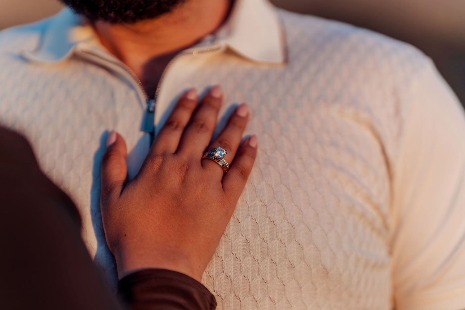 Close-up of a woman's hand with an engagement ring resting on a man's white textured sweater.