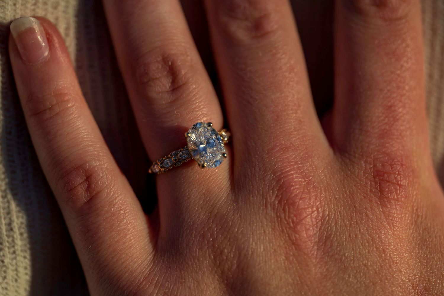 Close-up of a hand wearing a stunning gold engagement ring with a large oval diamond center stone and pavé band.