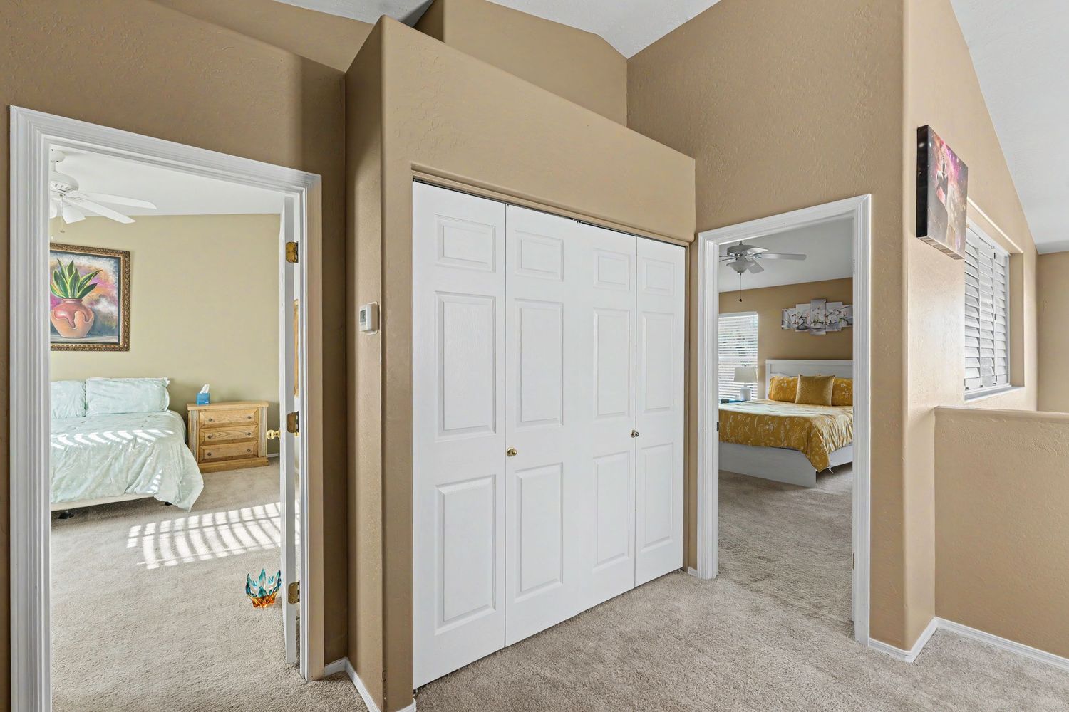 Hallway with white bi-fold closet doors and views into two carpeted bedrooms with ceiling fans.