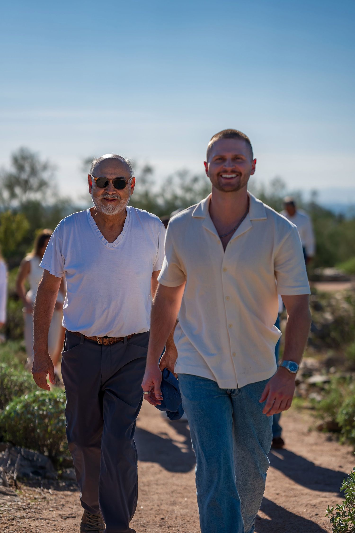 Two people walking and smiling on a desert trail with mountains in the background.
