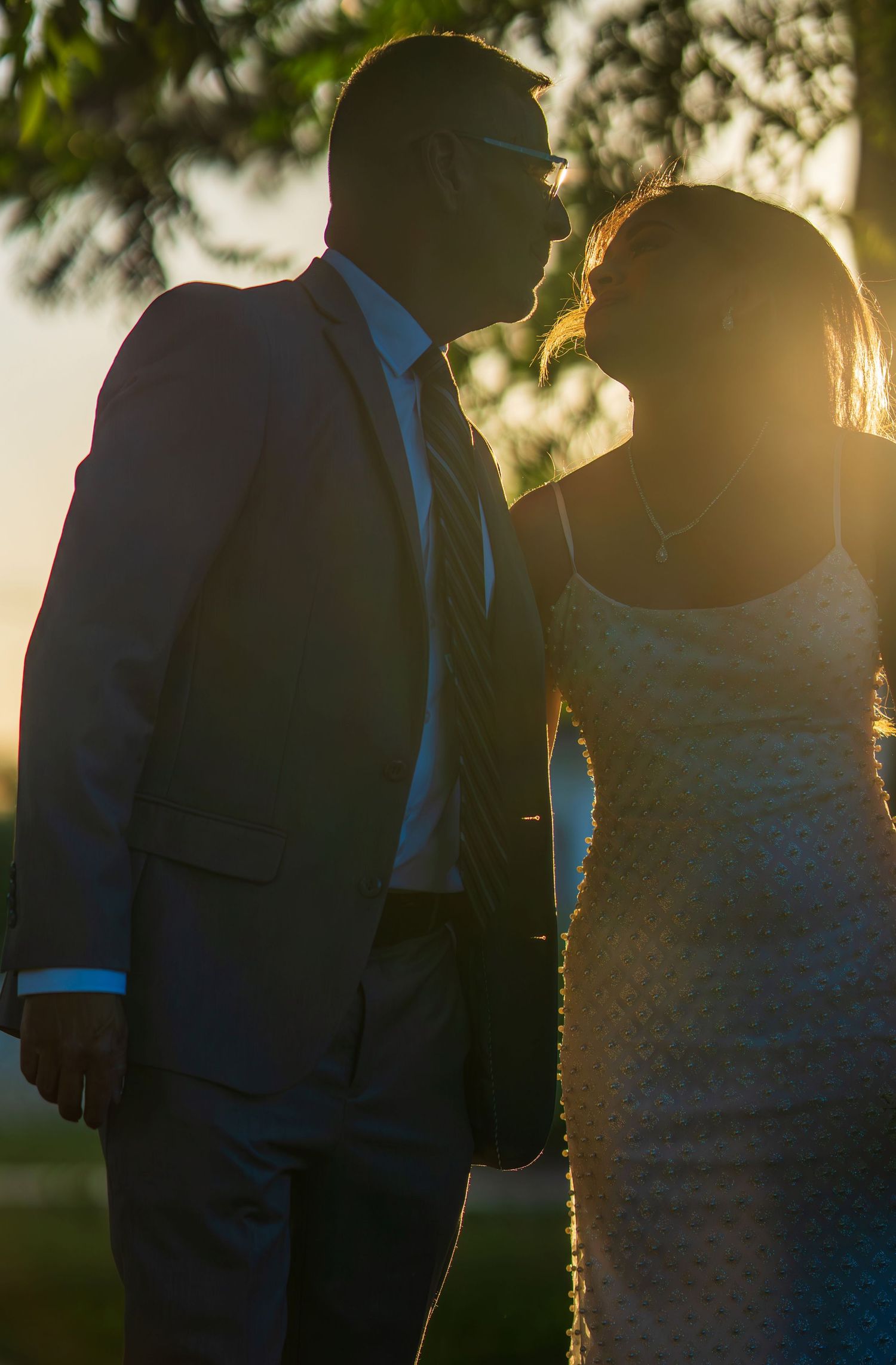 A couple shares a romantic silhouette moment at golden sunset with warm backlight glowing.