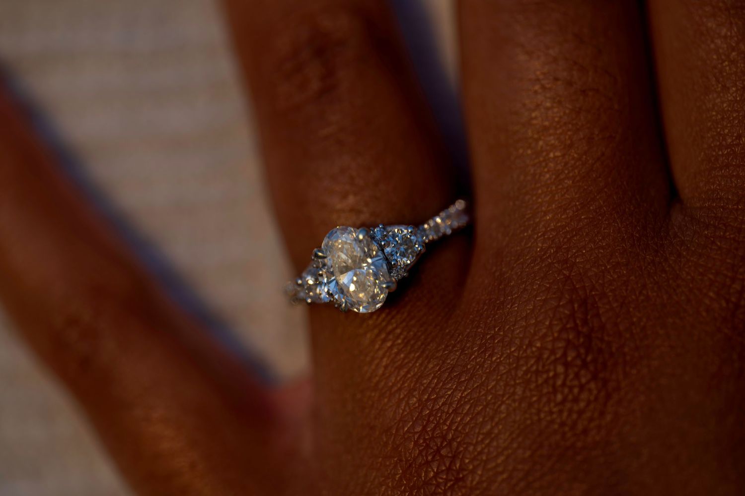 Close-up of a diamond three-stone engagement ring with pavé band on a dark-skinned finger.