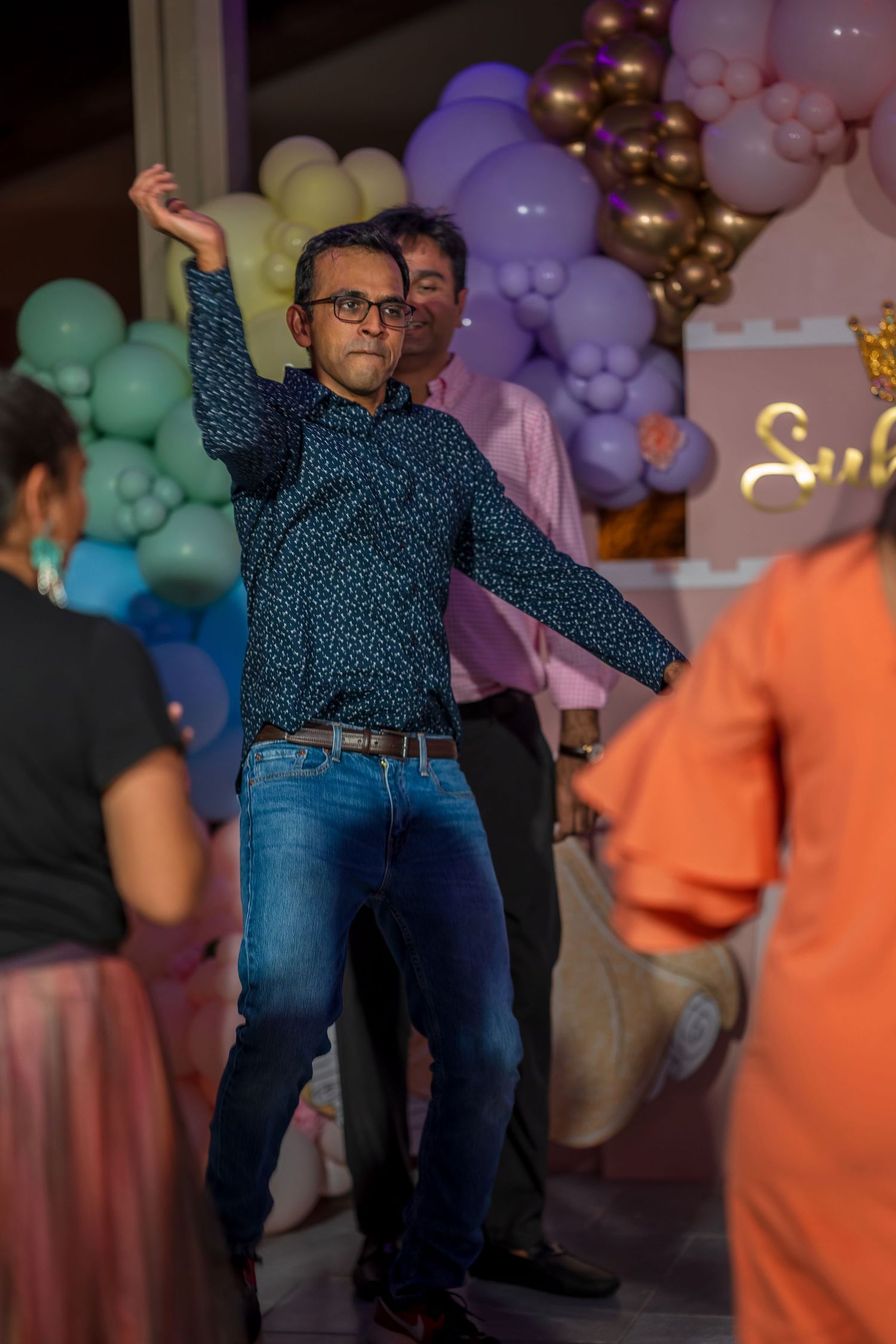 Party guests dancing energetically under colorful balloon decorations.