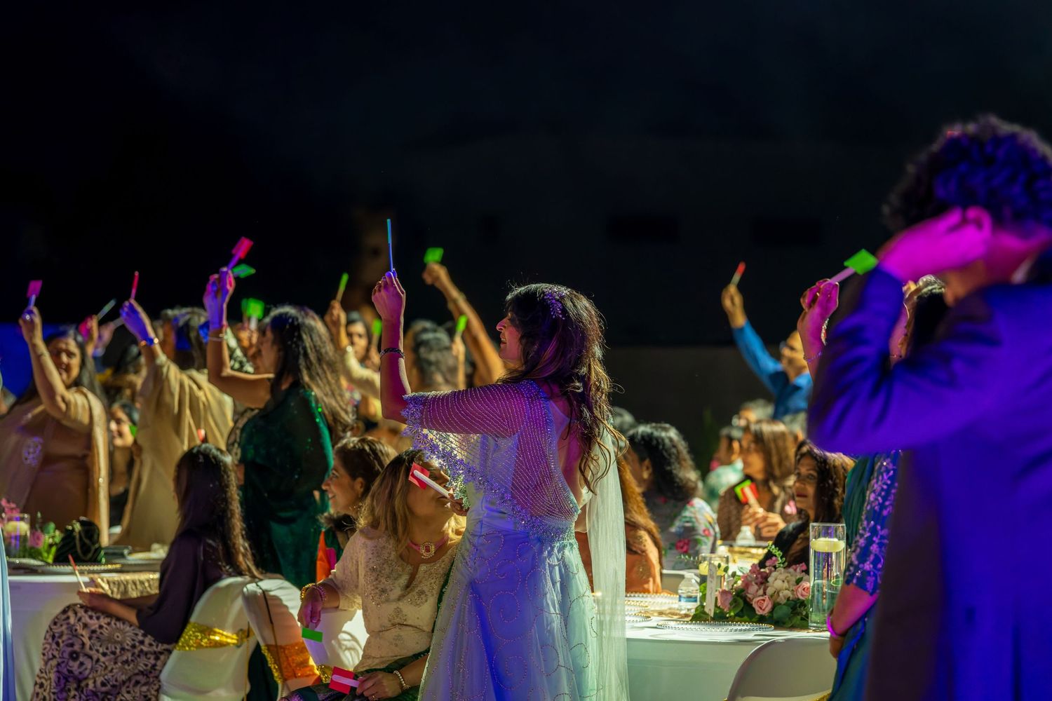 Guests dance and celebrate with raised arms at a nighttime outdoor gathering.