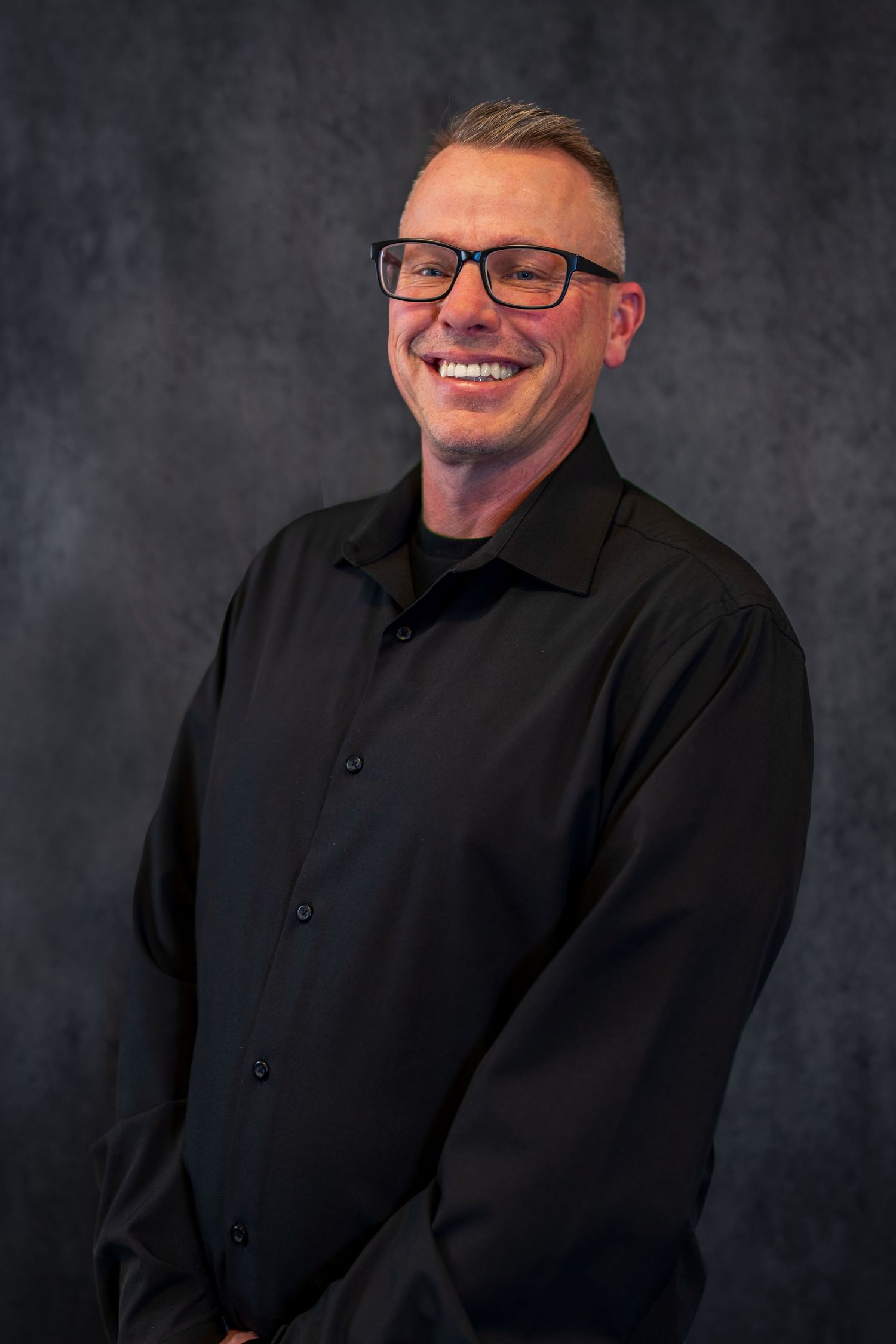 Professional studio portrait with glasses against dark background.