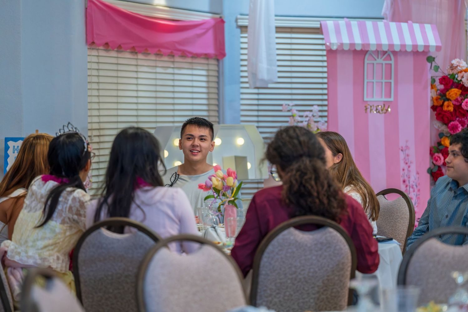 Celebration scene with pink decorations and partygoers seated at tables.