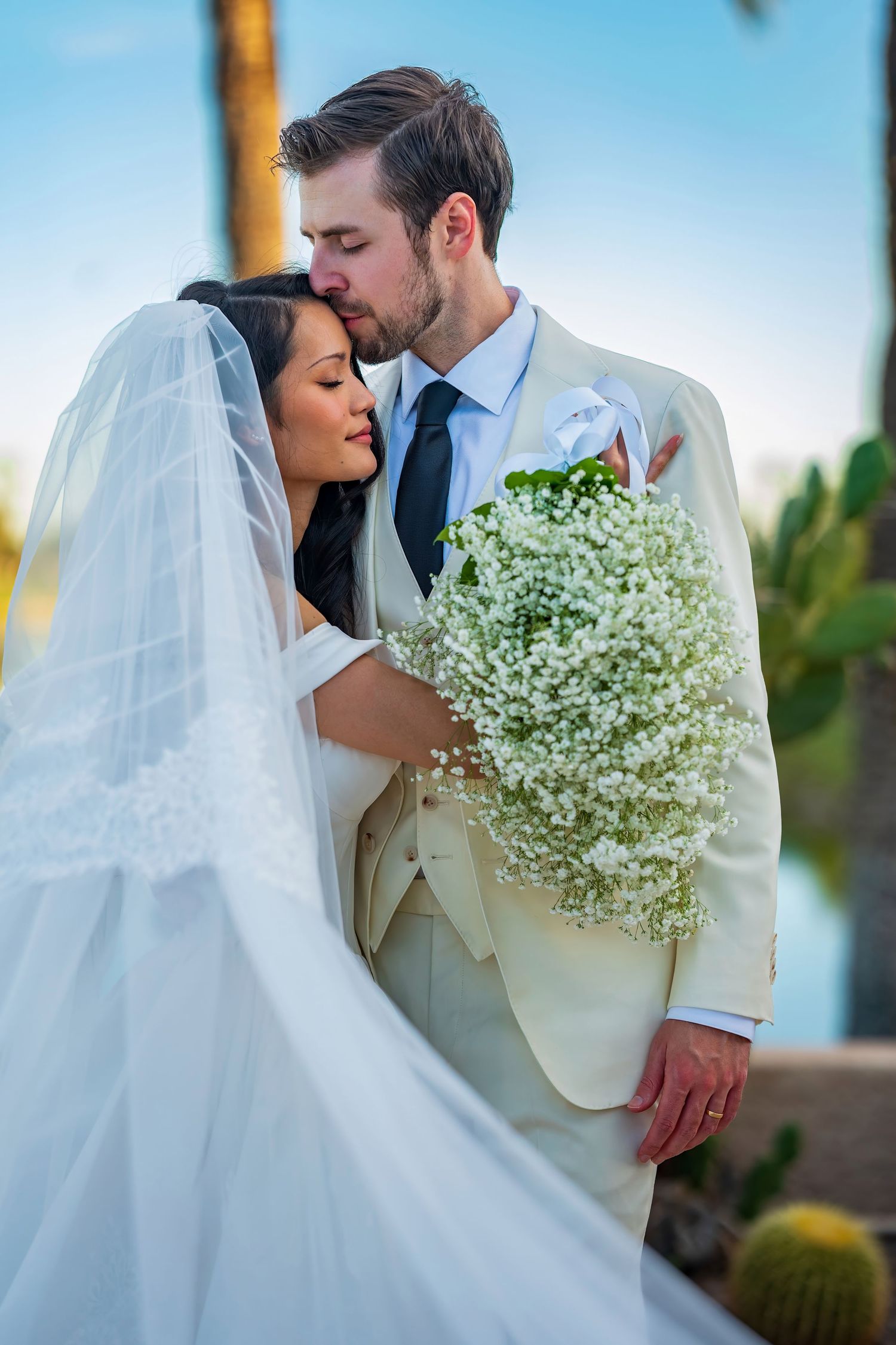 Newlyweds share intimate moment with baby's breath bouquet at outdoor venue.