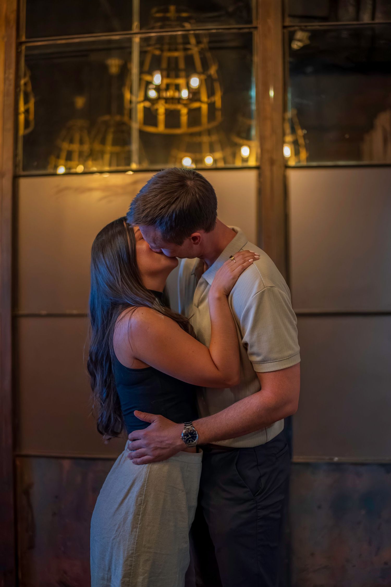 A romantic couple sharing an intimate embrace in a dimly lit restaurant with a chandelier visible in the background.