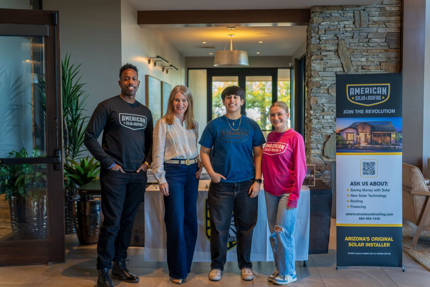 Team members standing together in office setting with American Solar Roofing display banner.