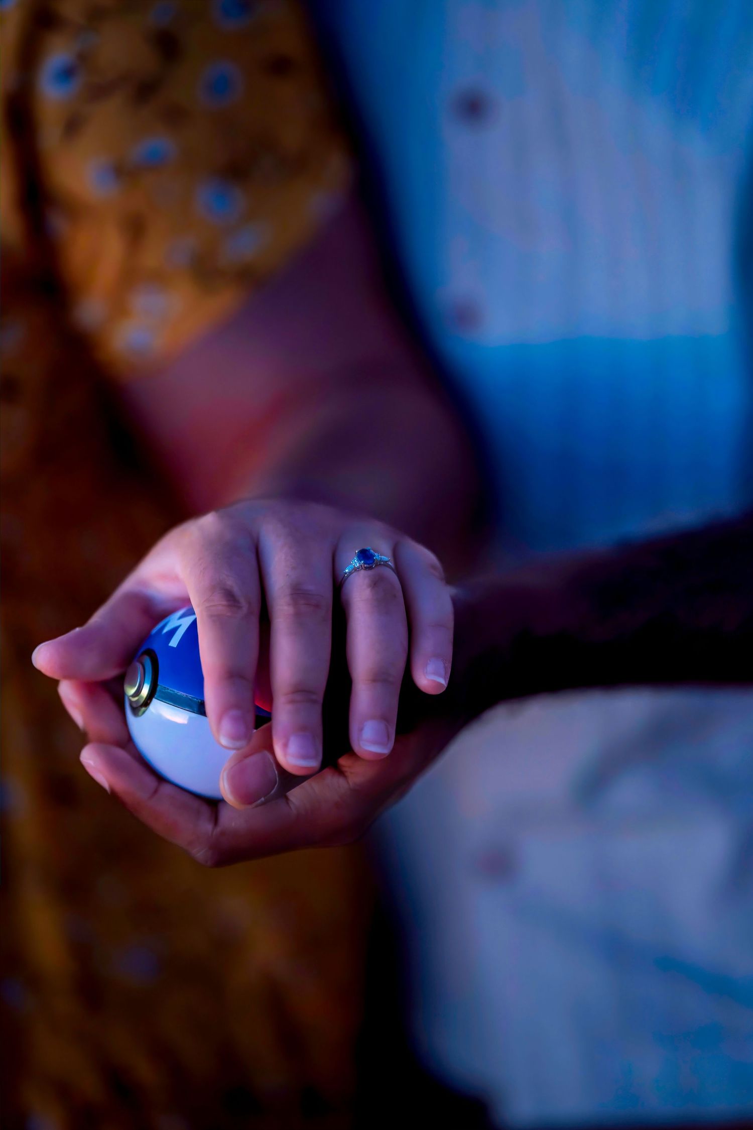 Hands holding a glowing blue Pokeball with an engagement ring visible on finger.