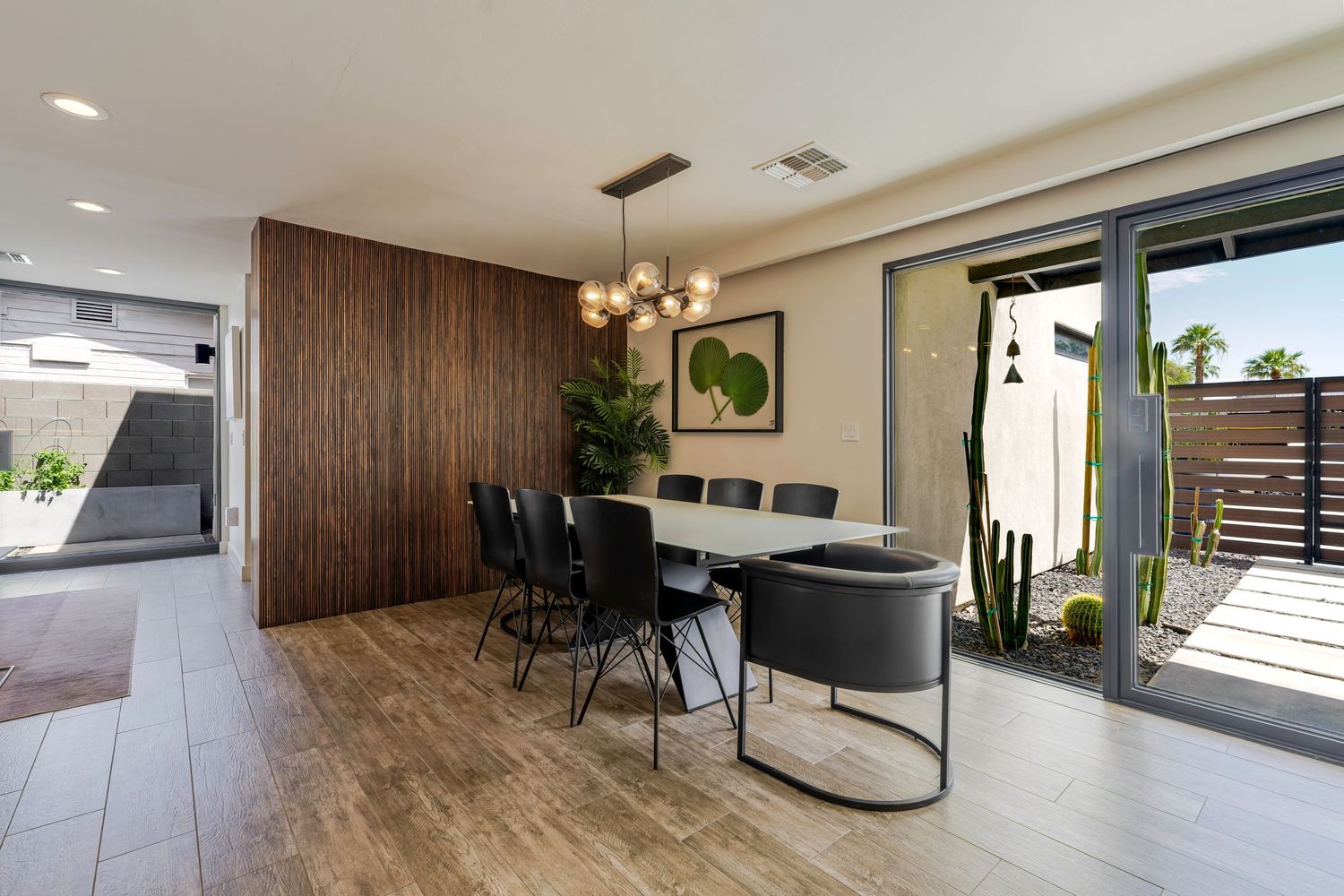 Contemporary dining room with wood accent wall, chandelier, black chairs, and sliding glass doors to patio.