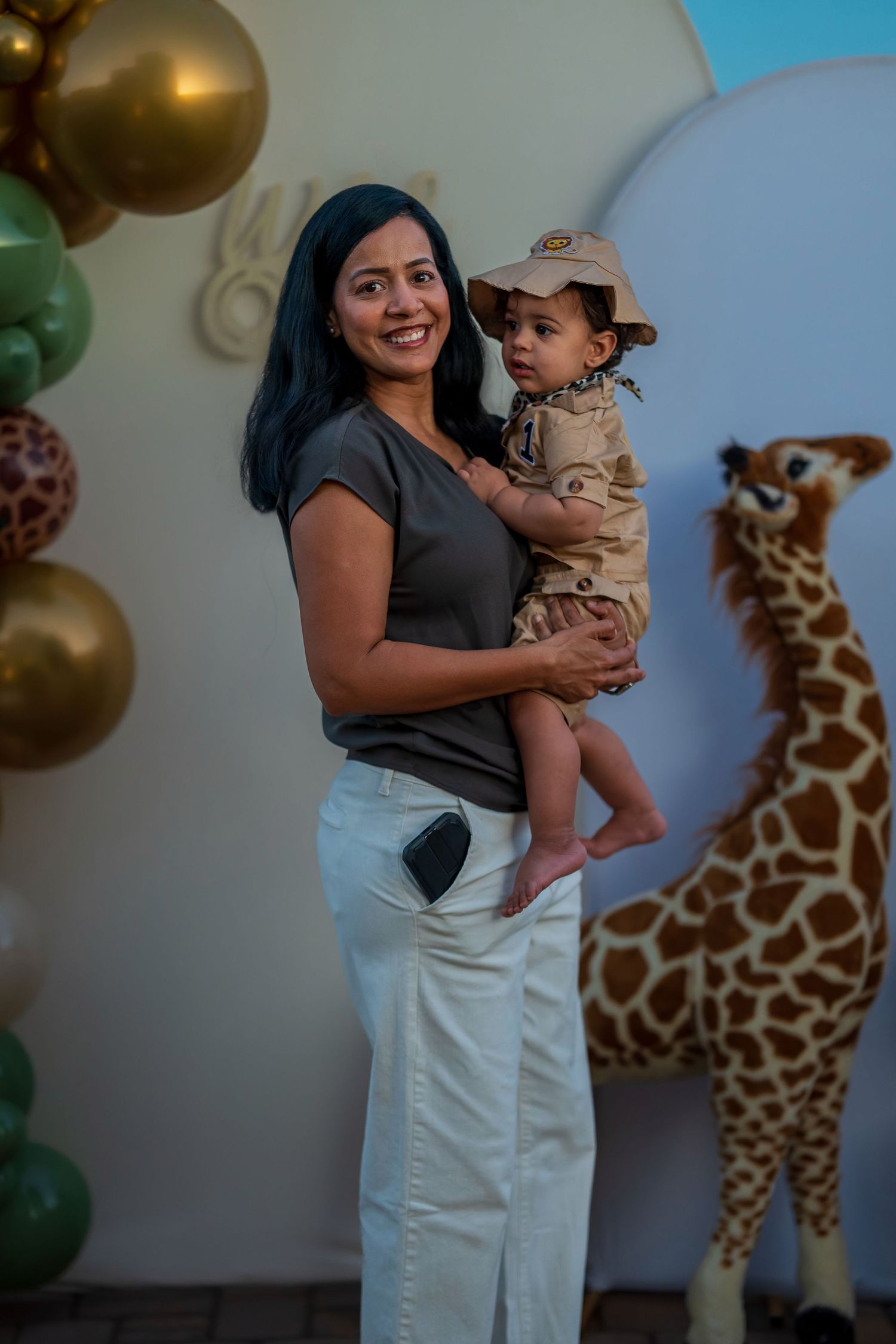 A family celebrates at a safari-themed party with giraffe decorations and gold balloons in the background.