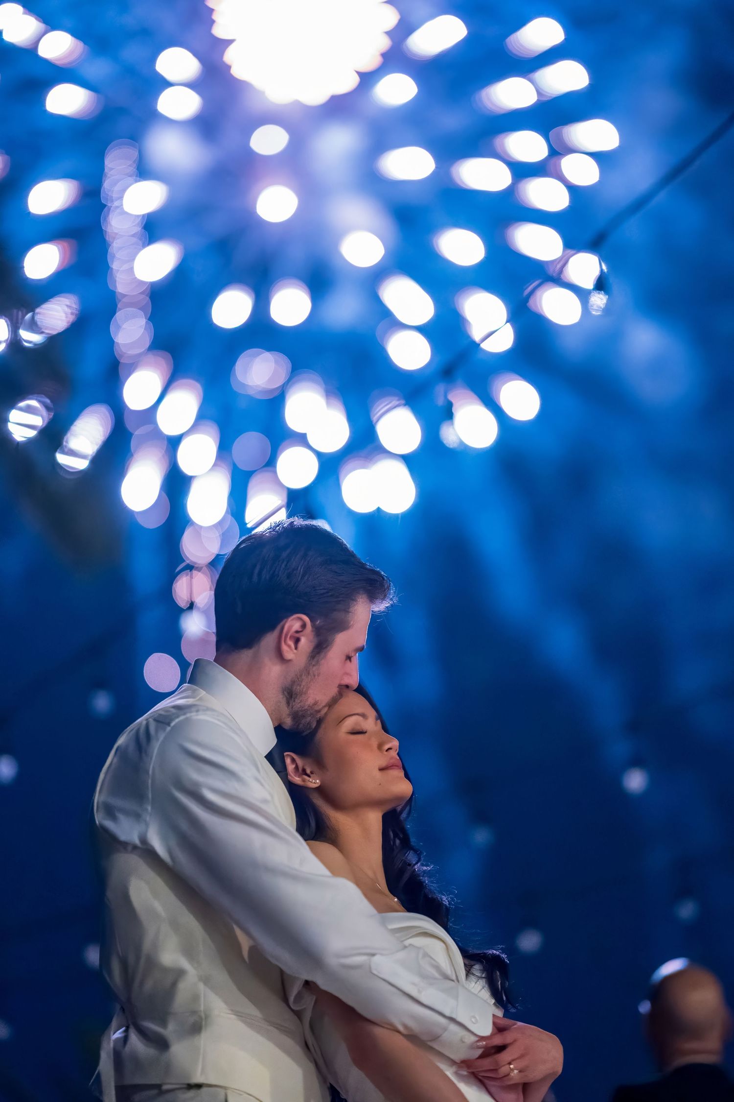 Wedding couple shares intimate moment under bright blue and white fireworks display.