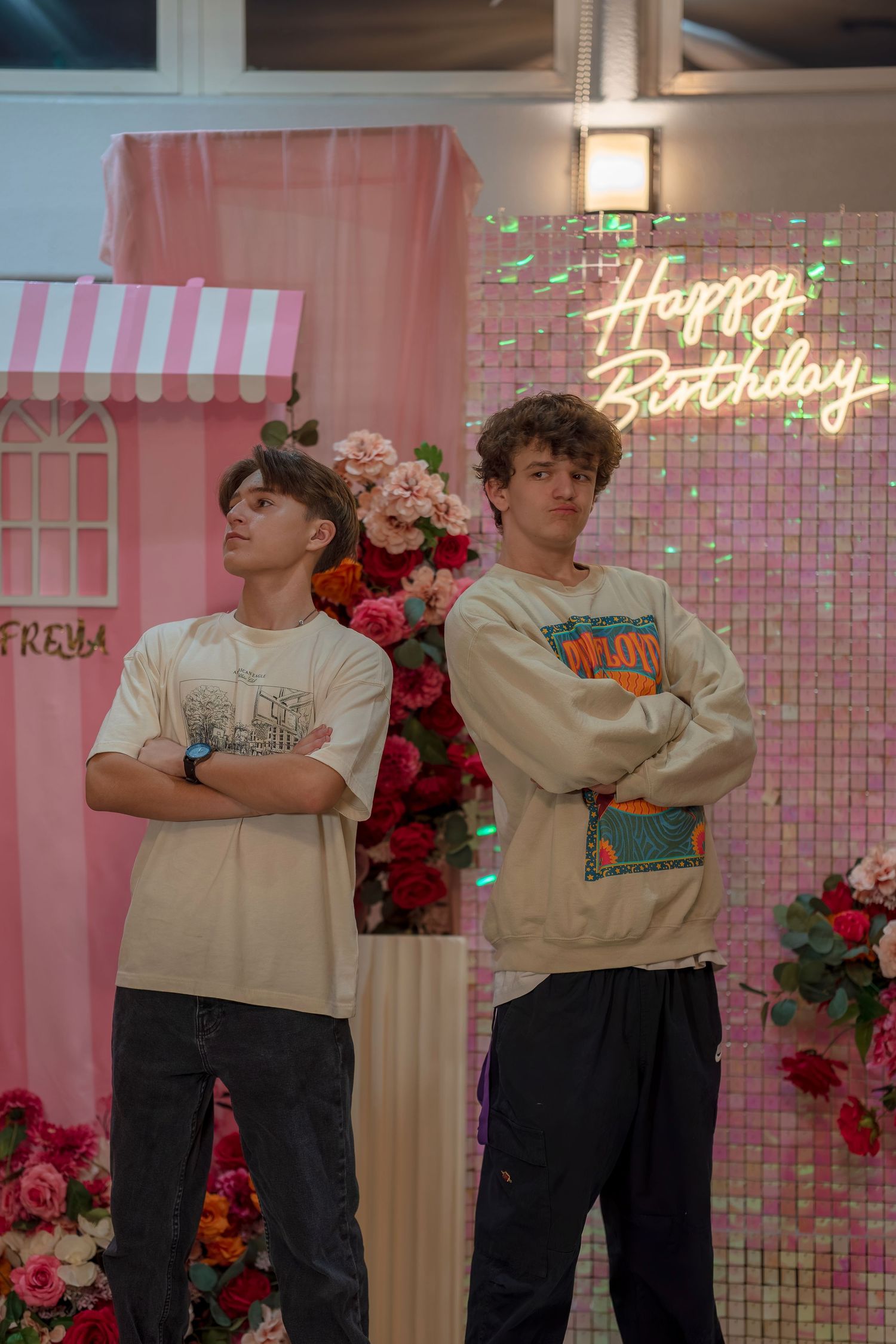 People posing in casual outfits against a pink backdrop with neon signs and floral decorations.
