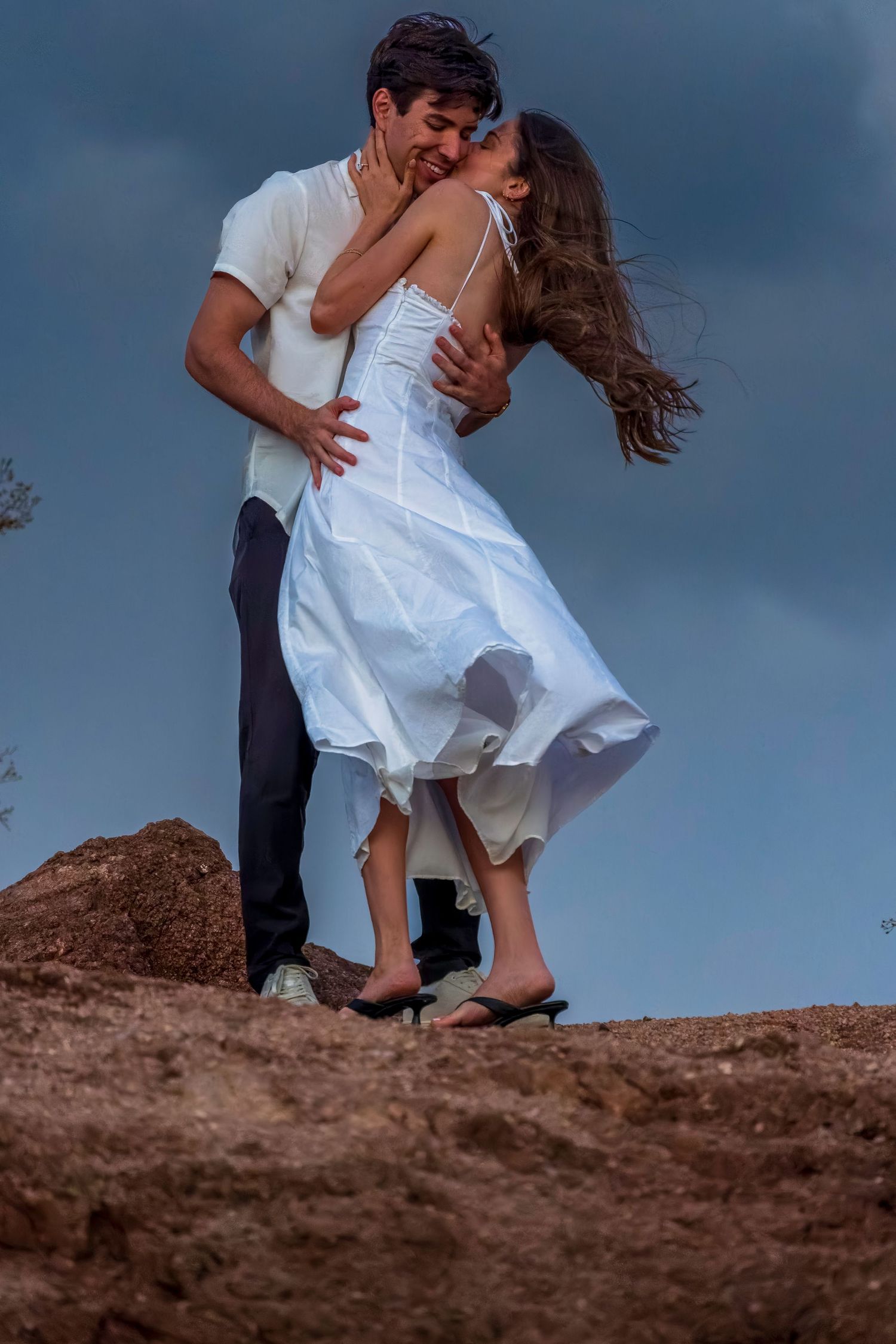 Dancing couple on rocky outcrop against stormy sky background.