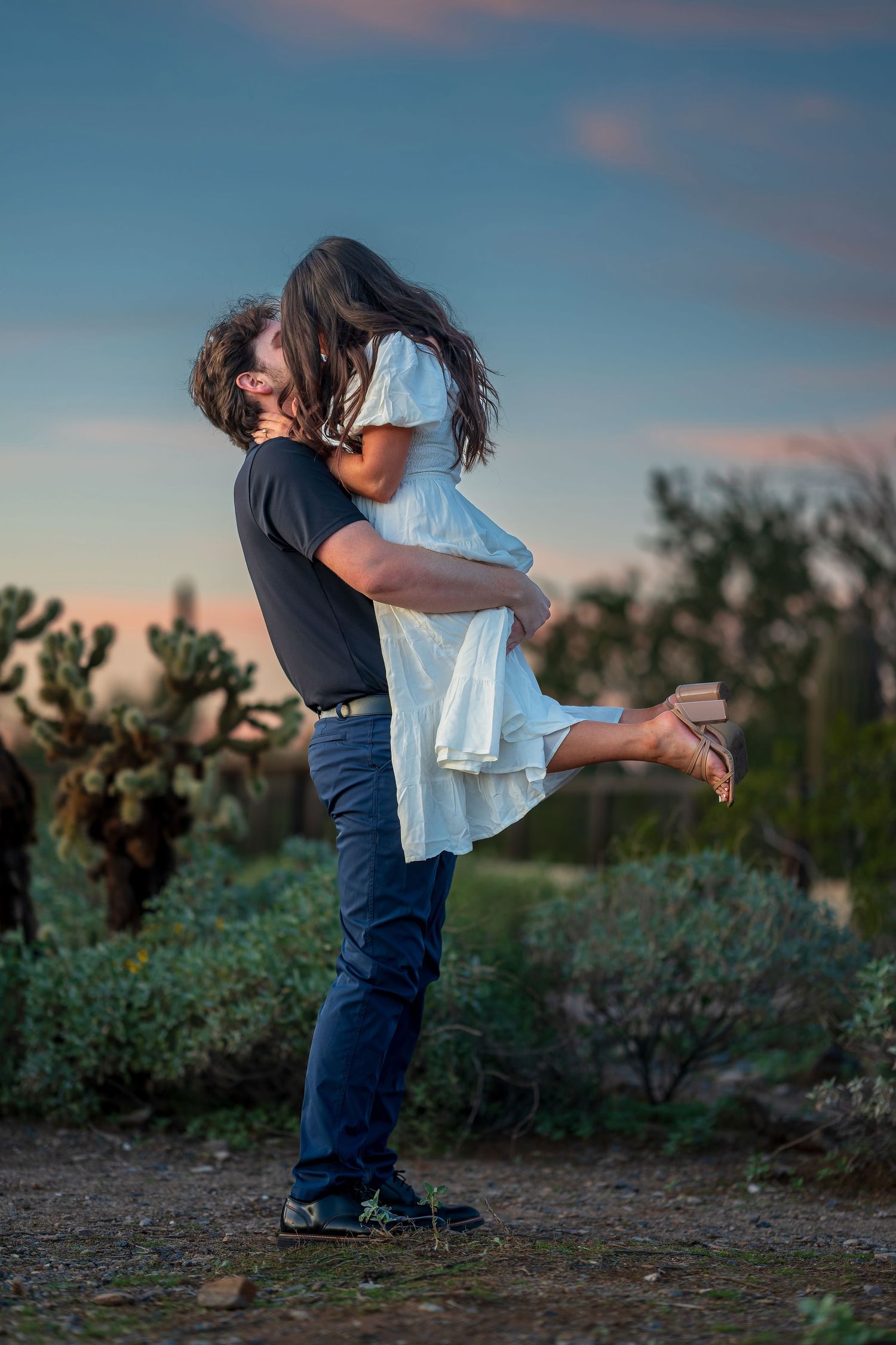 A romantic desert engagement photo featuring a dramatic dip pose at sunset.