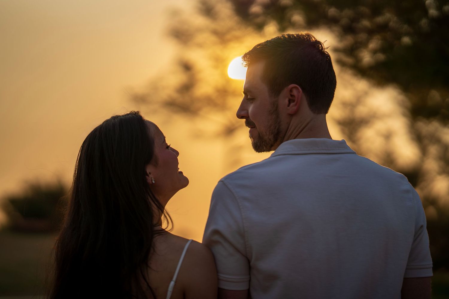 A couple gazes at each other romantically backlit by a warm golden sunset glow.