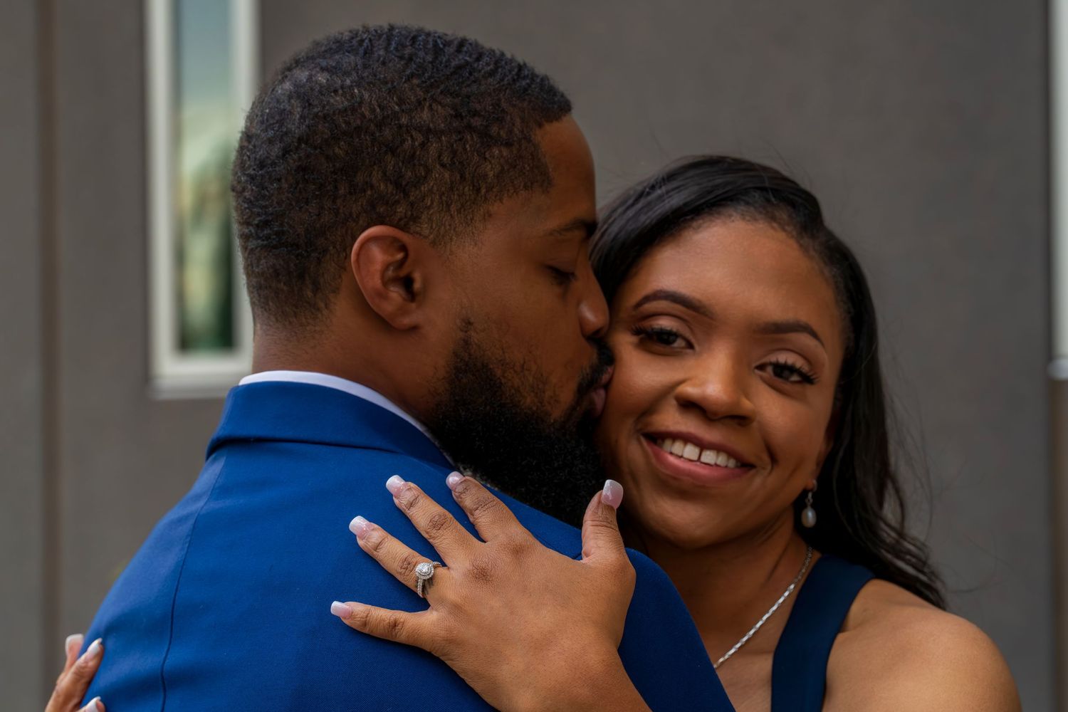 Groom in blue suit kissing bride on cheek as she smiles warmly during wedding celebration.