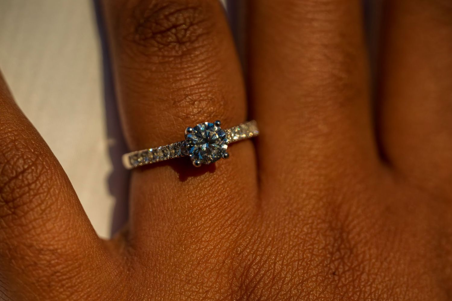 Close-up of a diamond solitaire engagement ring on a dark-skinned woman's finger.