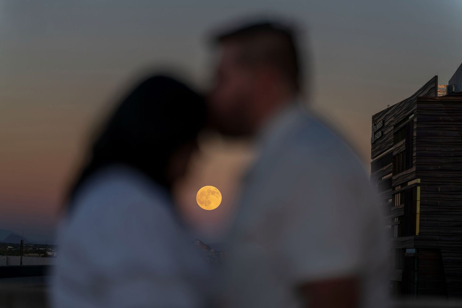 Silhouettes of buildings against a sunset sky with a full moon rising in the background.