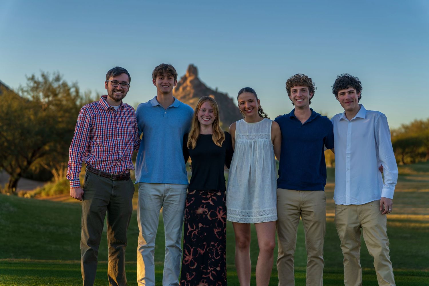 Family group photo taken outdoors at sunset with blue sky and natural backdrop.