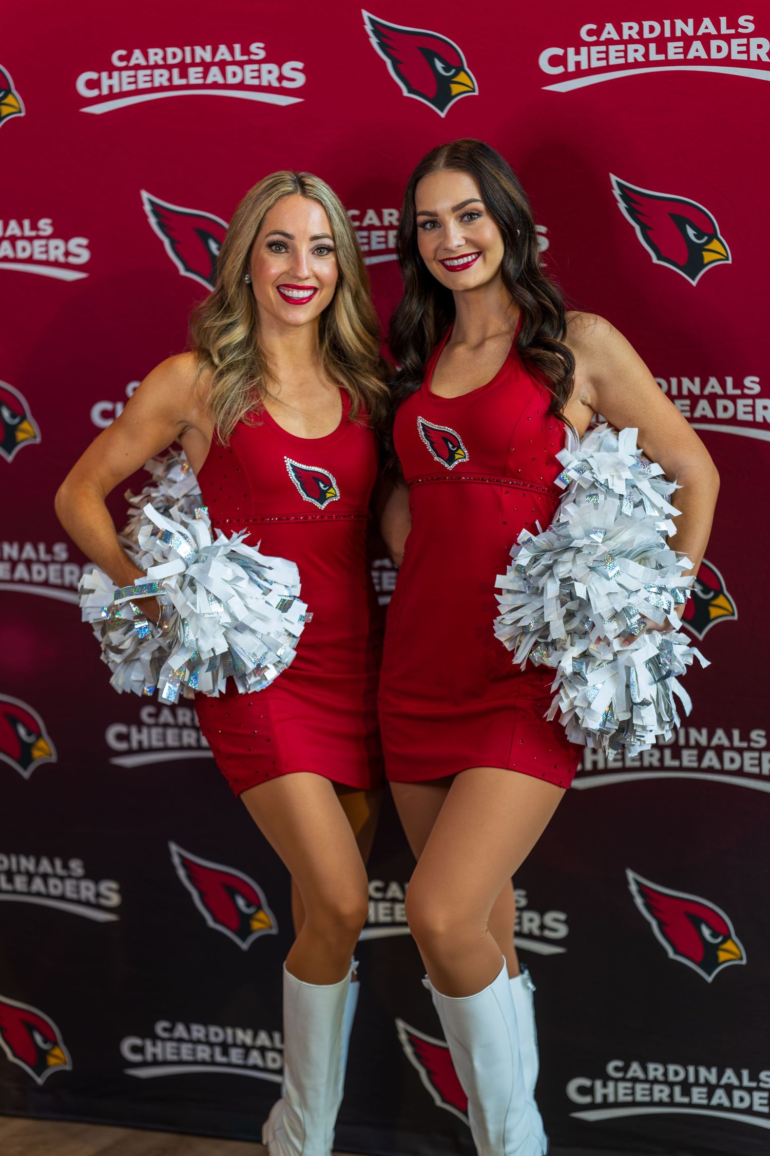 Cardinals cheerleaders in red uniforms and white boots pose against team backdrop.