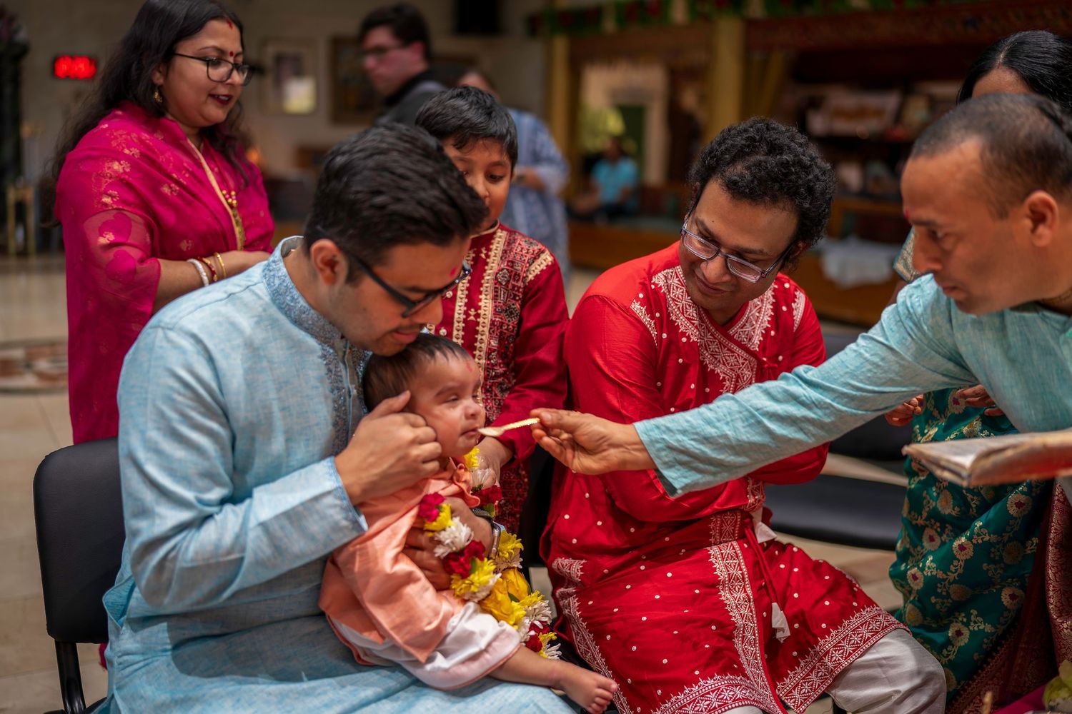 Indian family ceremony with adults in traditional attire performing a ritual with a baby dressed in festive clothing.