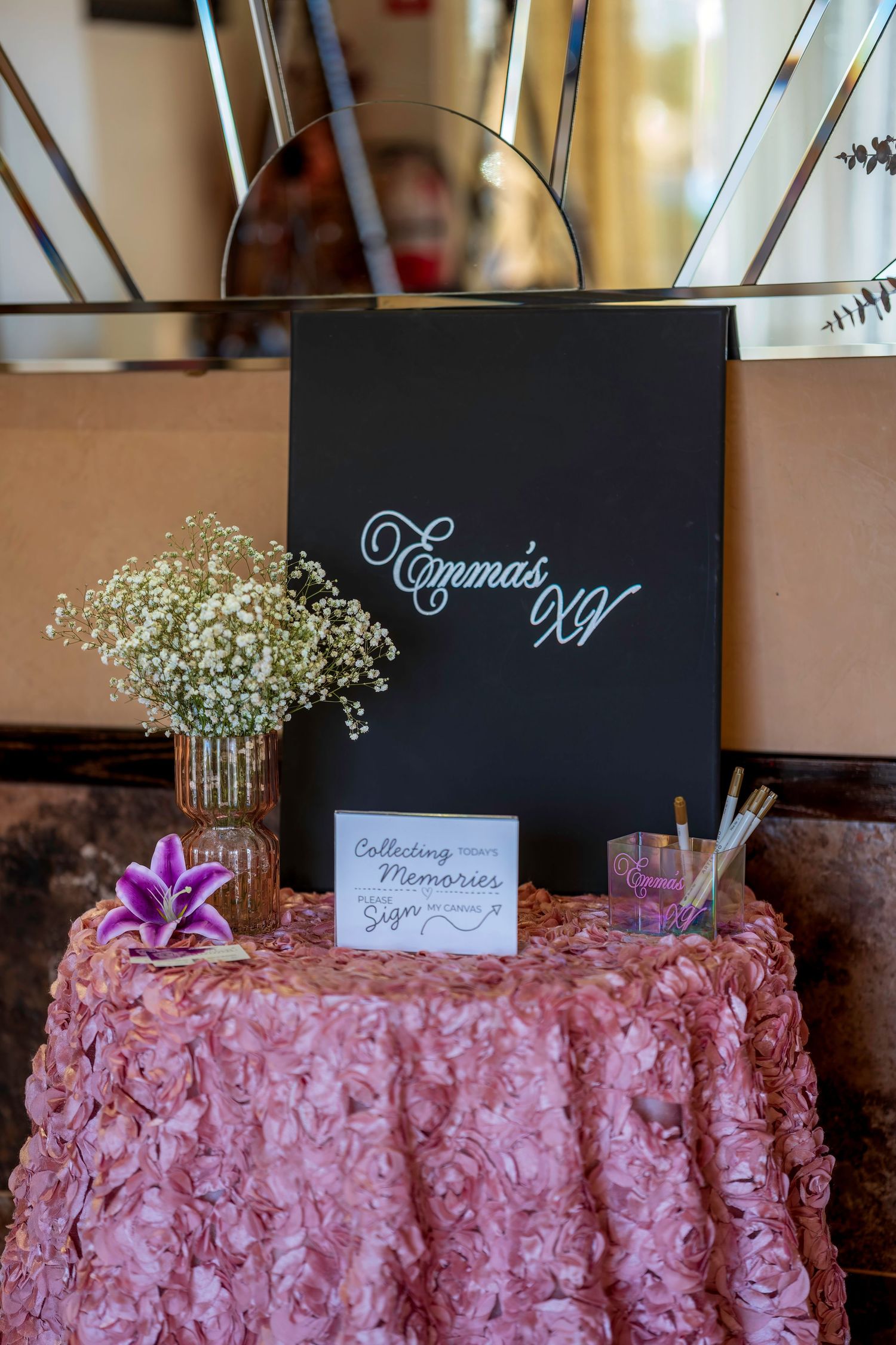 Emma's XV quinceañera sign-in table with floral decor, baby's breath, and a memories guest book on a pink rosette tablecloth.