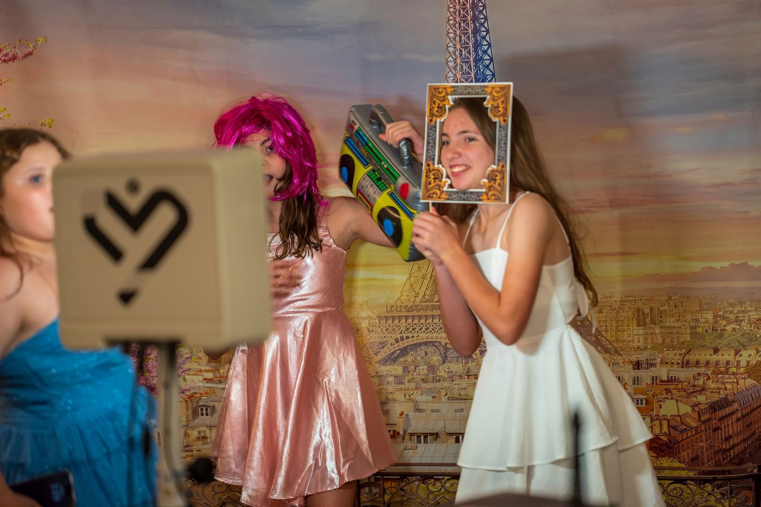 Girls in colorful dresses pose with fun photo booth props at a festive party celebration.