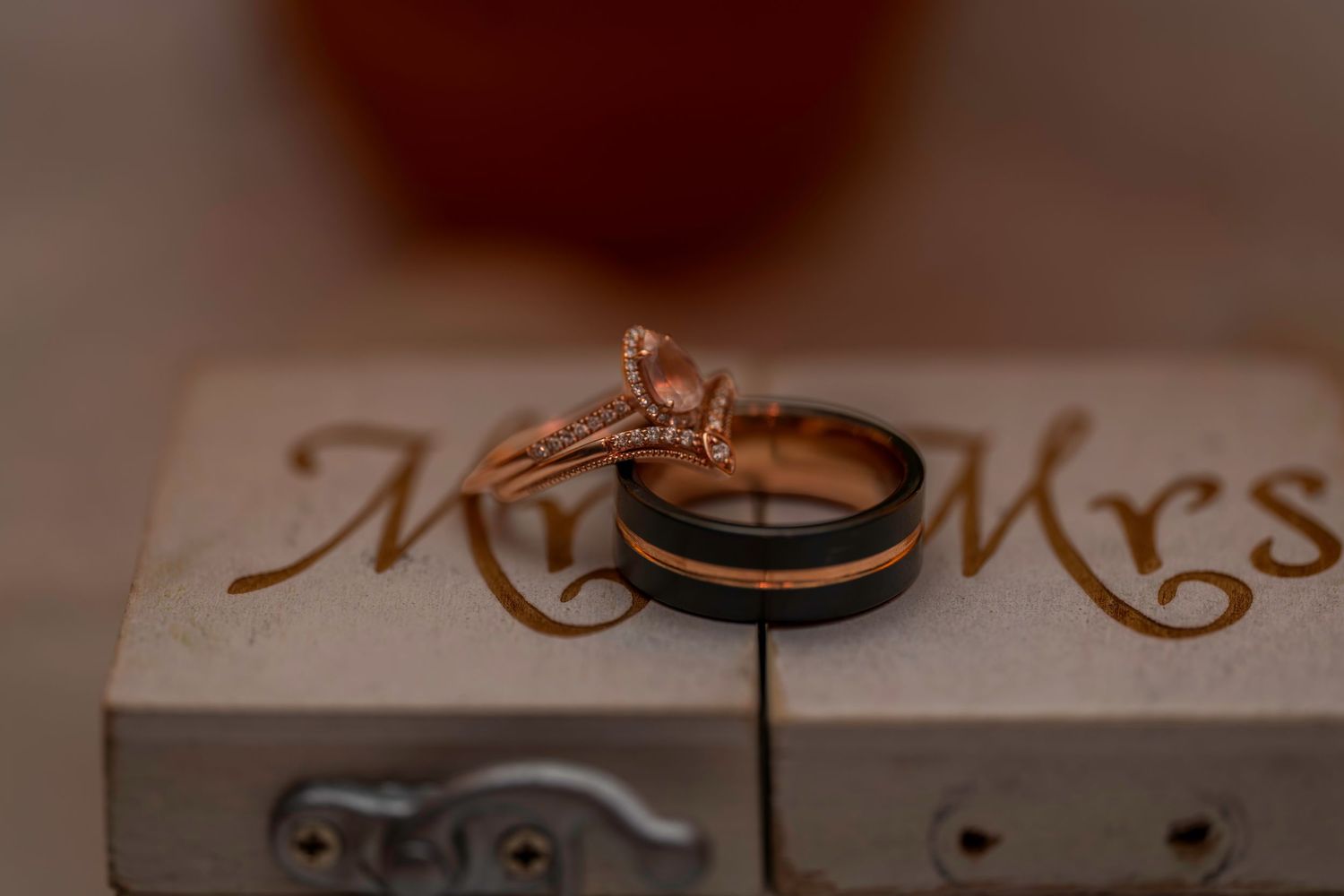 Rose gold diamond engagement ring and black wedding band displayed on Mr. and Mrs. ring box.