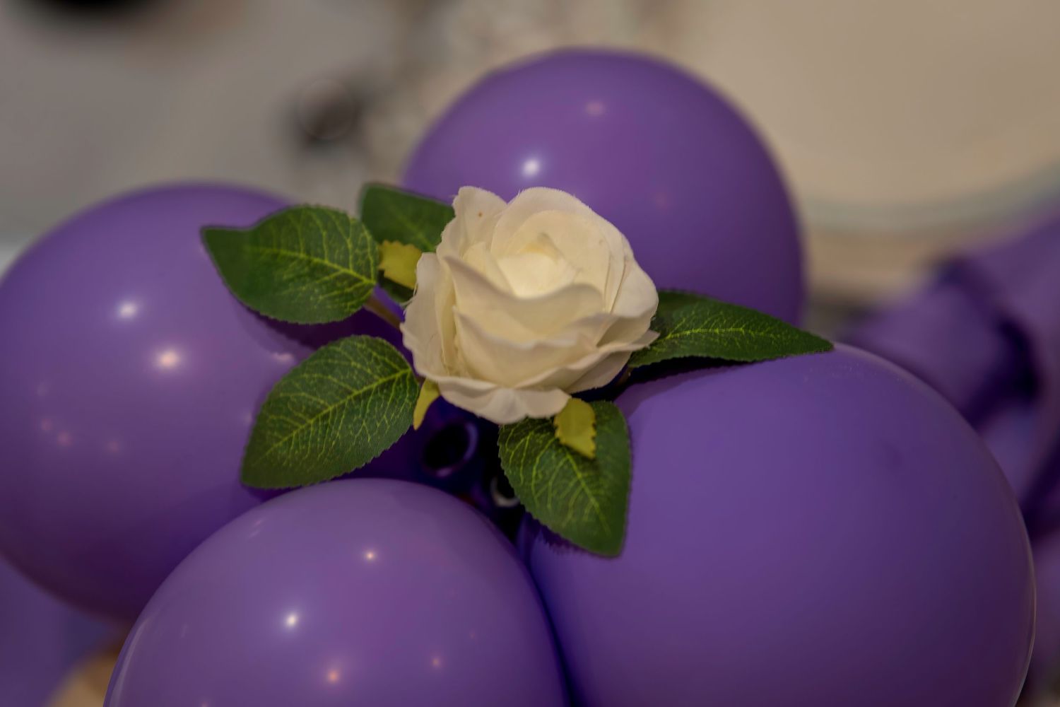Purple balloons decorated with a white rose and green leaves centerpiece arrangement.