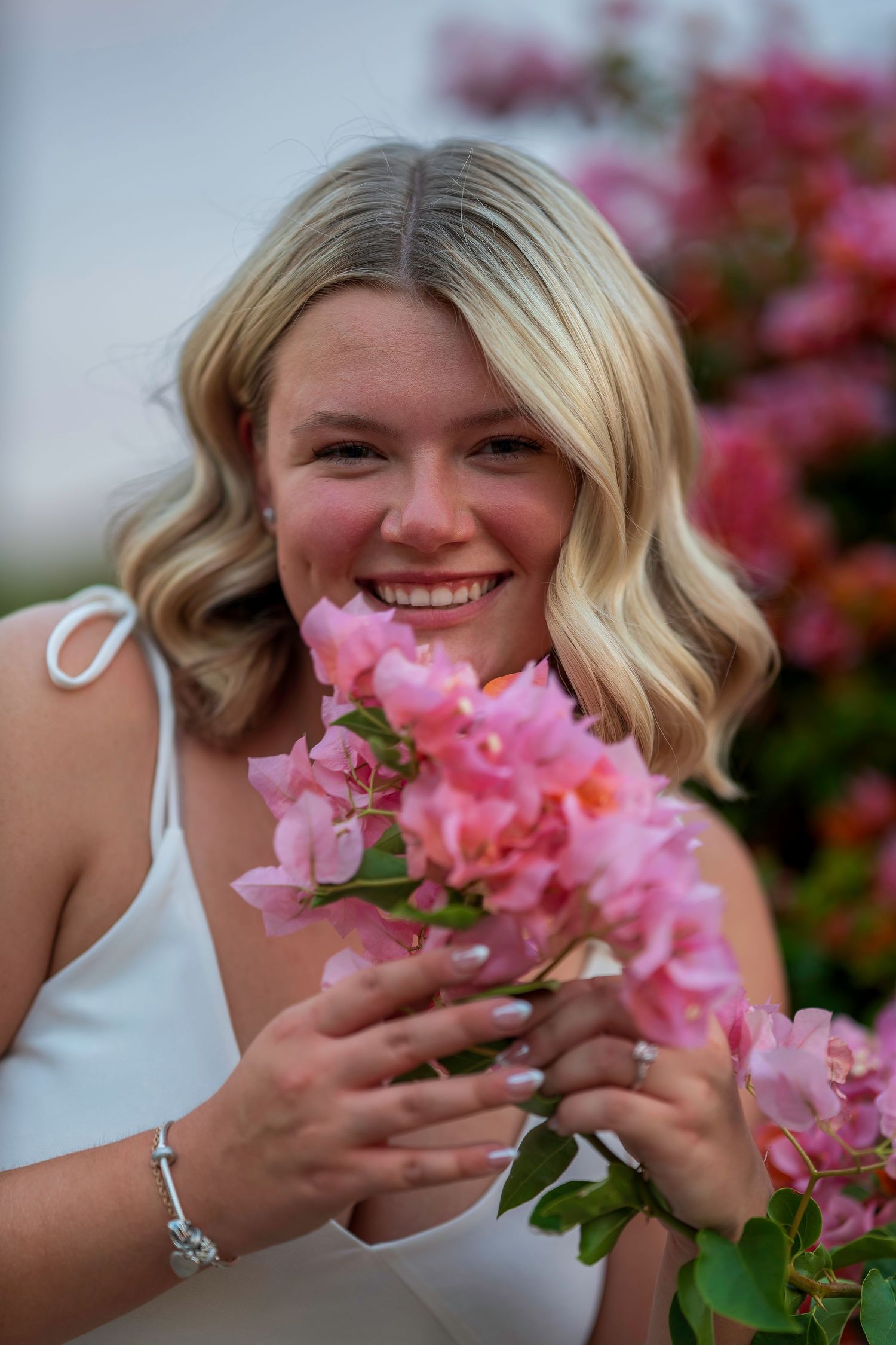 Happy blonde woman smelling pink bougainvillea flowers outdoors.