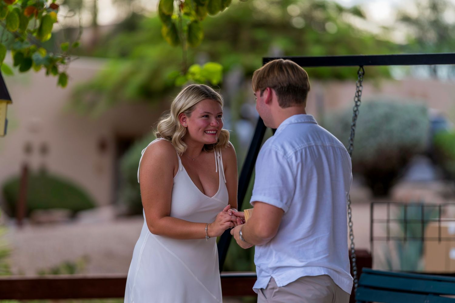 Couple smiling and holding hands during an outdoor marriage proposal near a decorative swing.