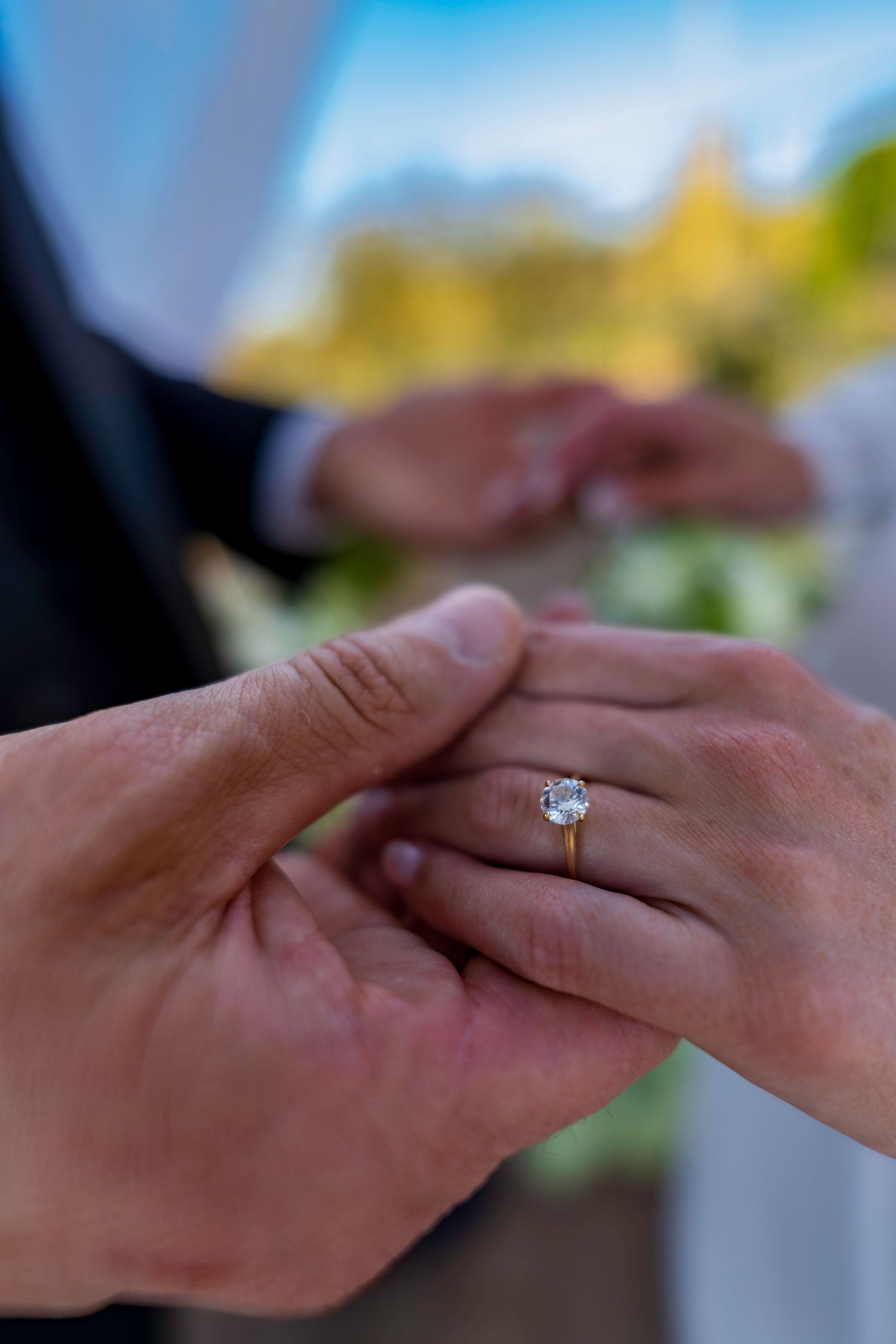 Close-up of groom placing oval diamond solitaire engagement ring on brides finger at wedding.