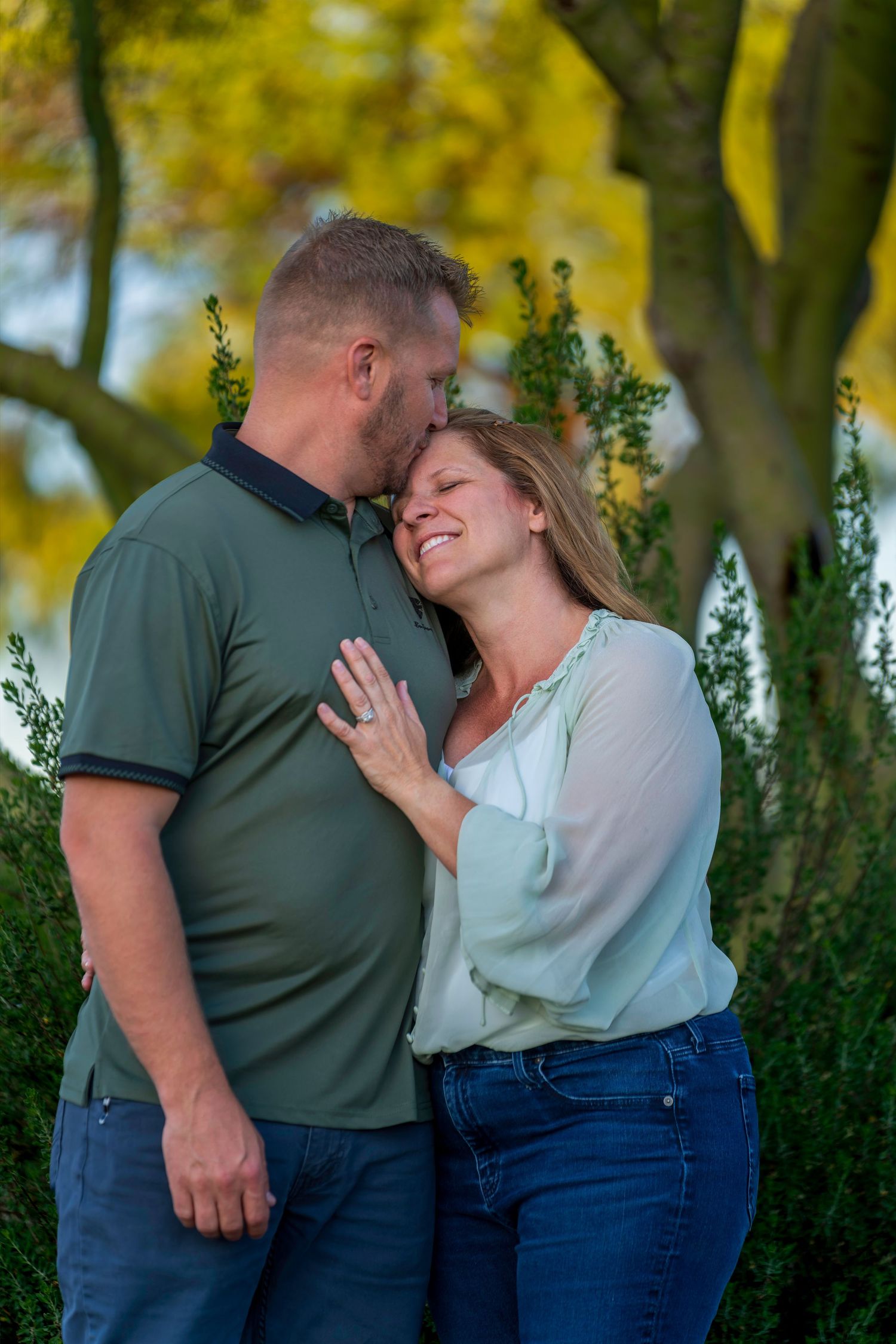 A happy couple embraces and laughs together in a scenic outdoor setting with vibrant yellow trees in the background.