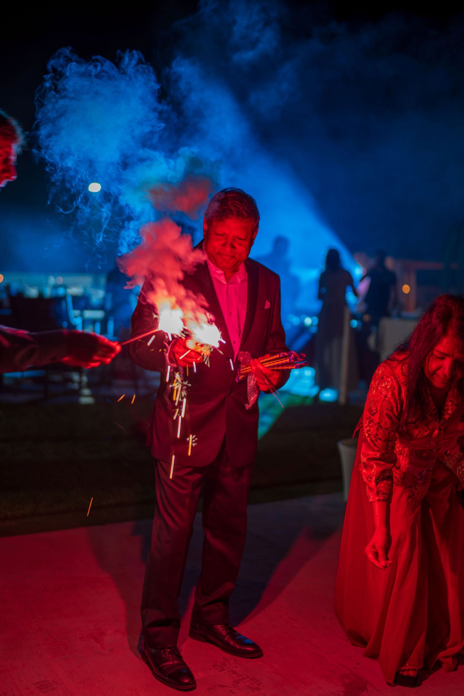 Red and blue smoke creates dramatic lighting effects at an outdoor nighttime celebration.