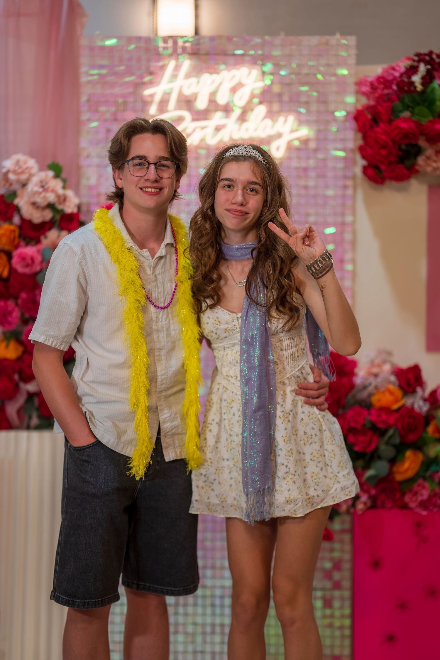 Party attendees wearing yellow scarves and casual attire pose in front of a pink floral wall.