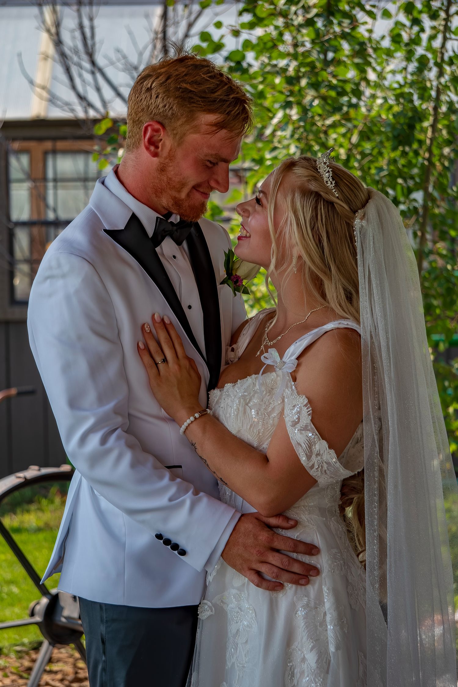 Intimate wedding portrait of a couple embracing under green foliage.