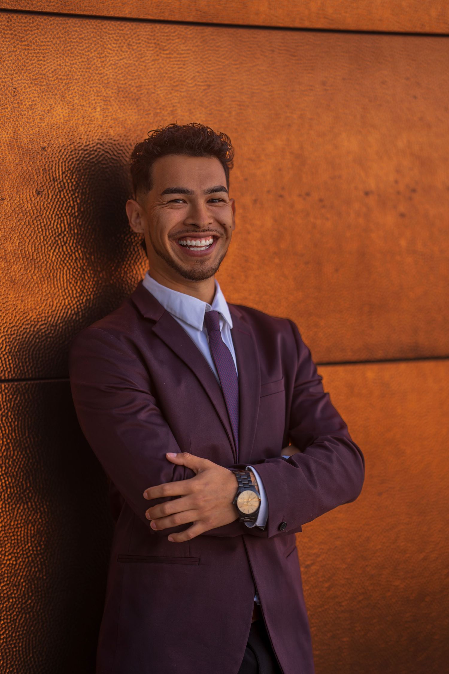 Professional portrait against orange wall showing confident pose in purple suit.