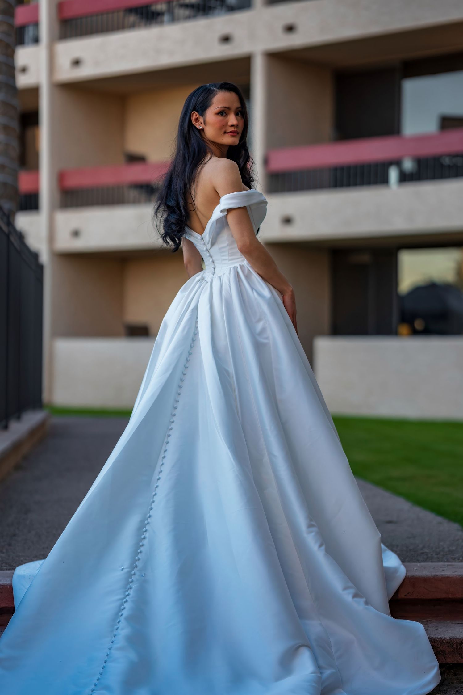 A bride in an off-shoulder ballgown poses outdoors showing the dramatic silhouette of her dress.