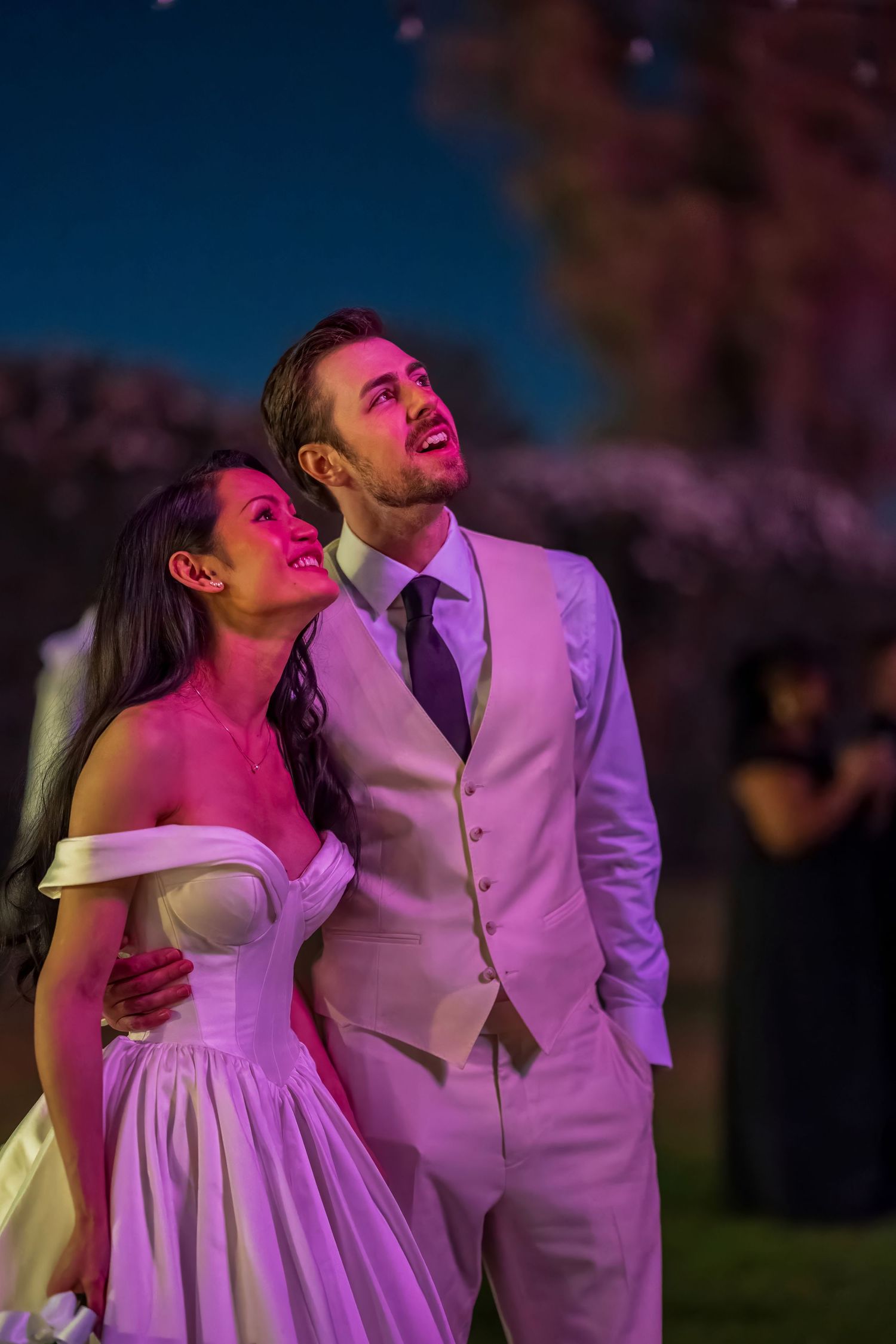 Wedding couple illuminated by pink and purple lights during evening celebration.