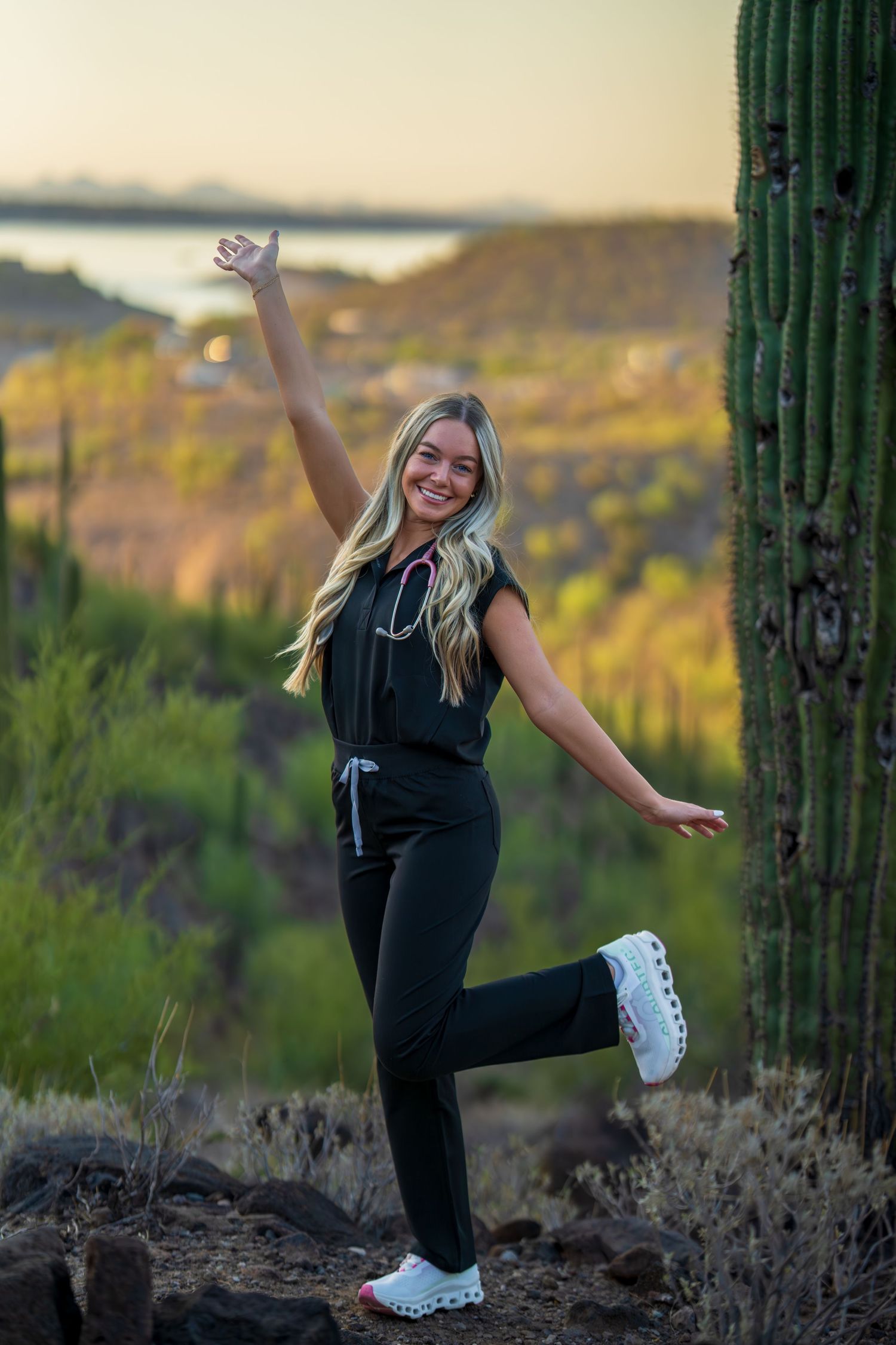 Energetic medical professional jumps and poses near saguaro cacti in desert setting.