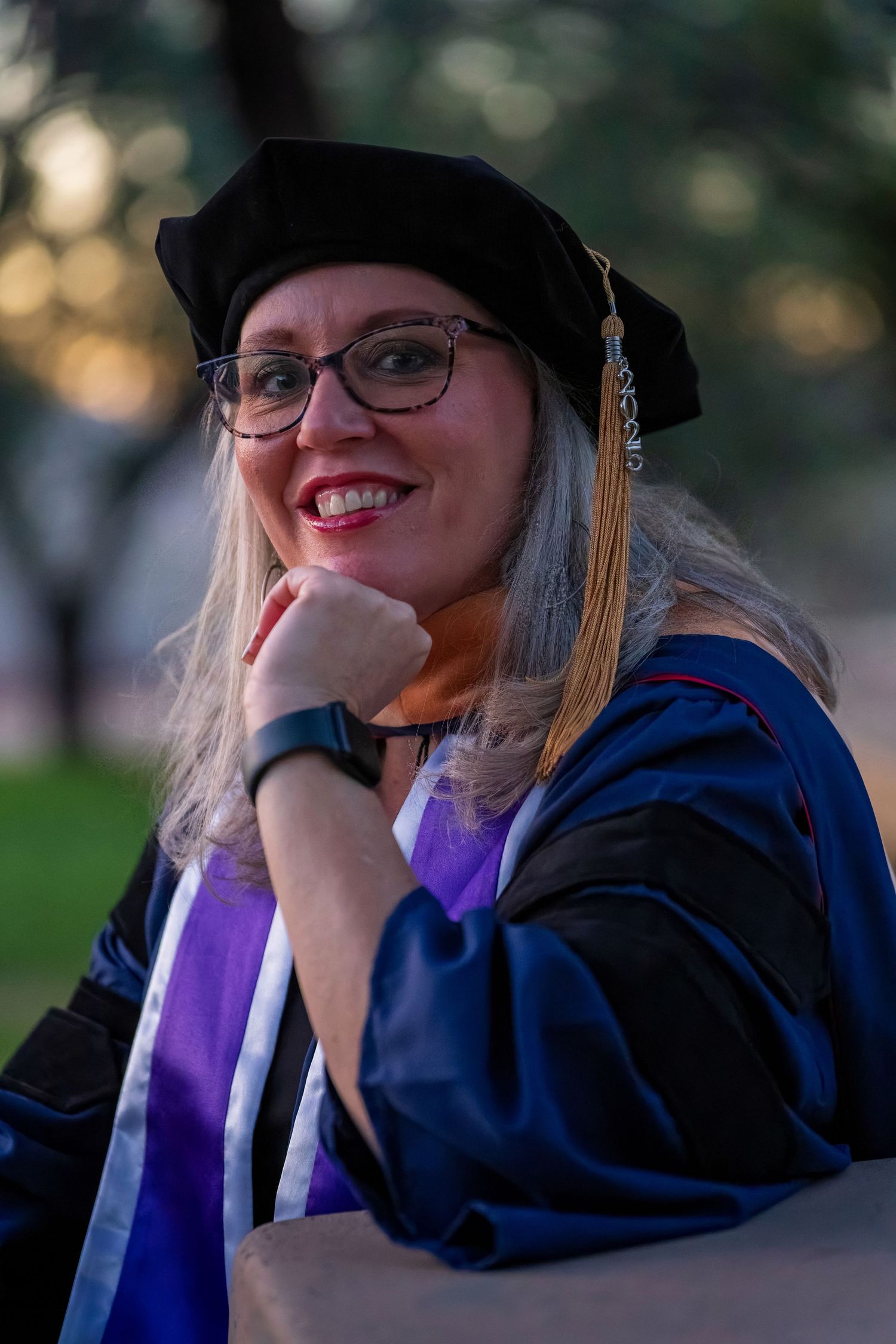 Graduate in cap and gown poses thoughtfully during sunset graduation photoshoot.