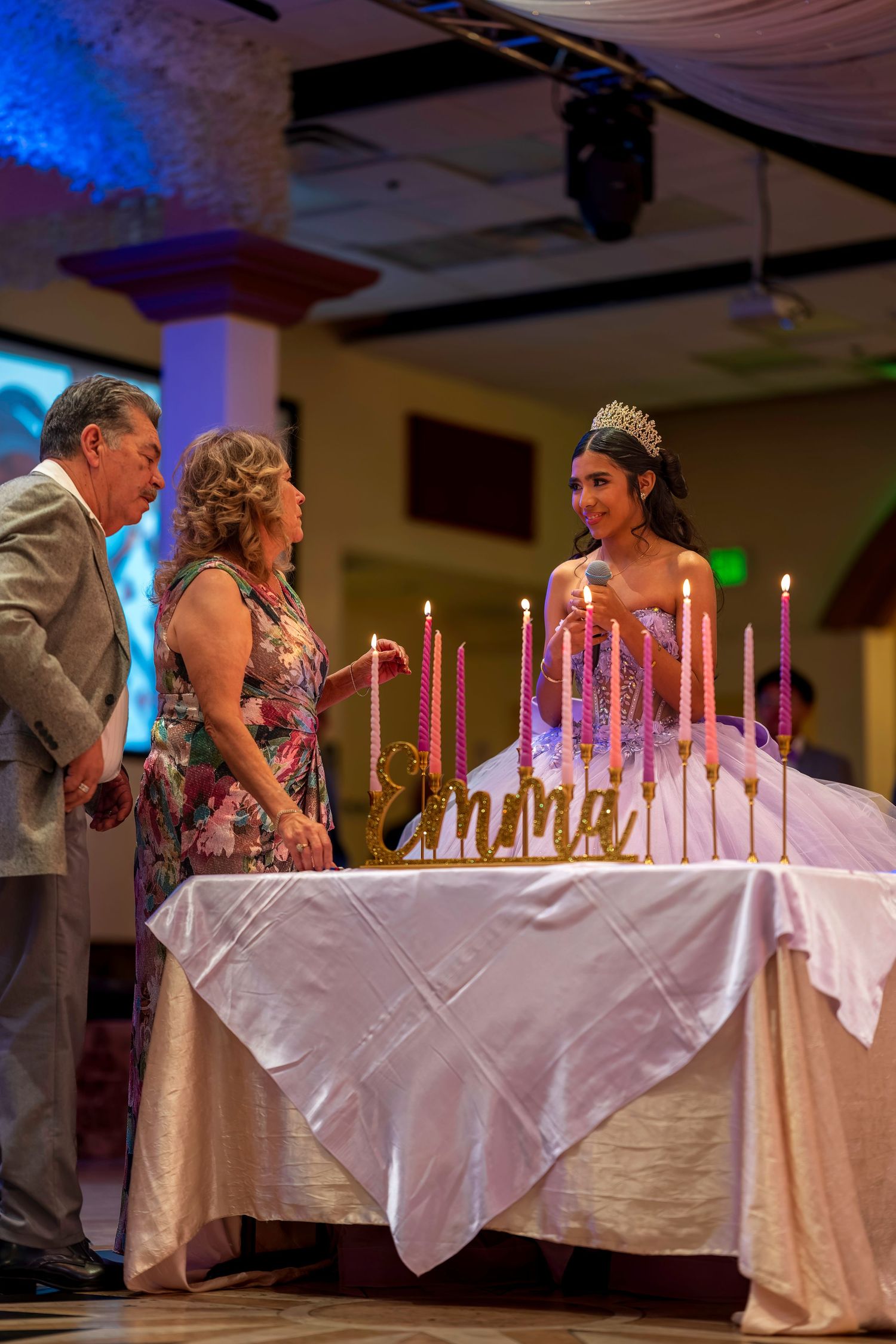 Young woman in tiara celebrates quinceañera with candle lighting ceremony at elegant banquet hall.
