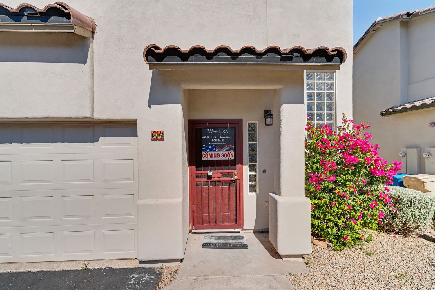 Southwest-style townhome entrance with red wood door, glass block window, blooming bougainvillea, and attached garage in Arizona.