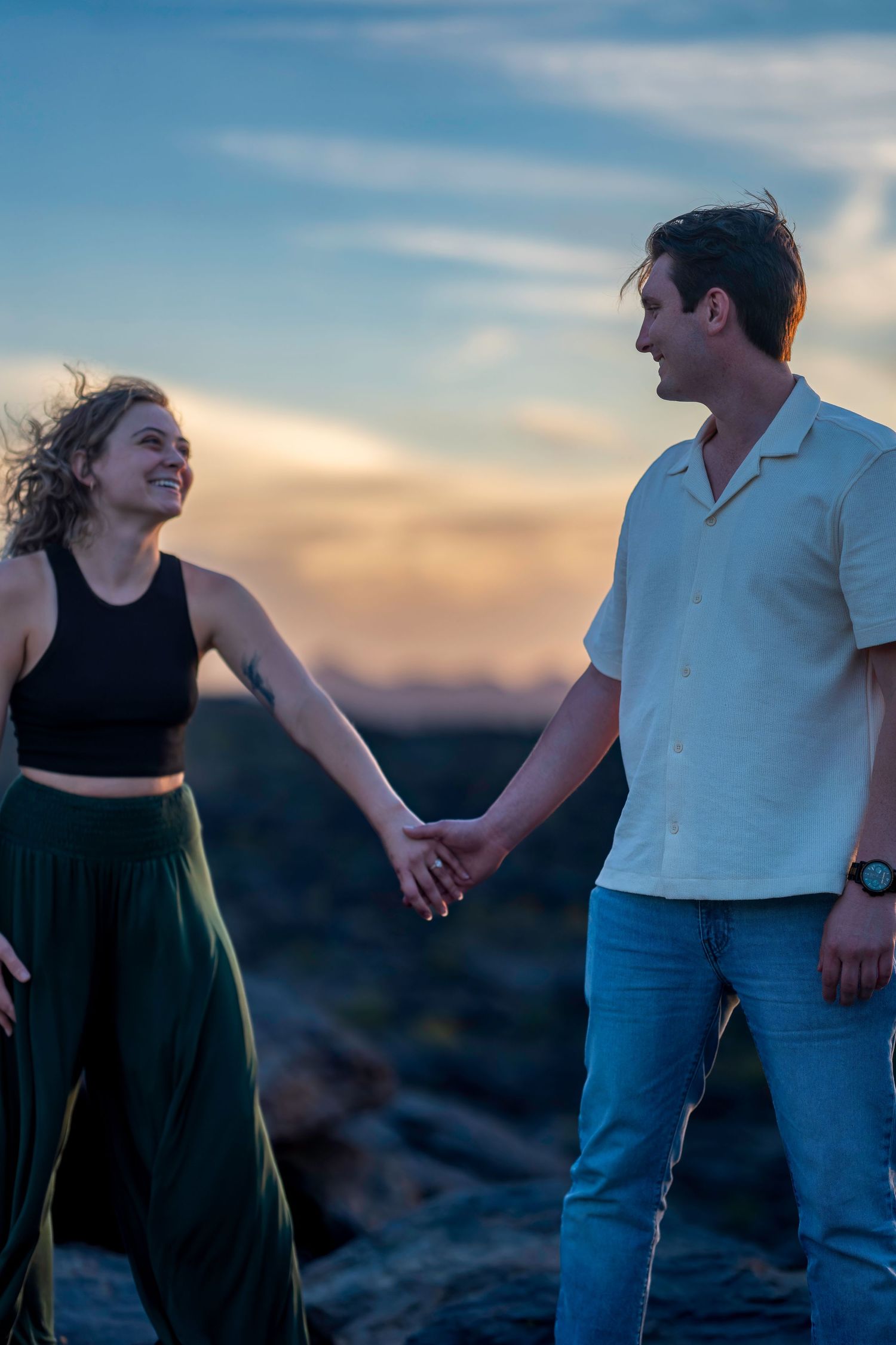 Happy couple holding hands and smiling at each other during a stunning outdoor sunset.