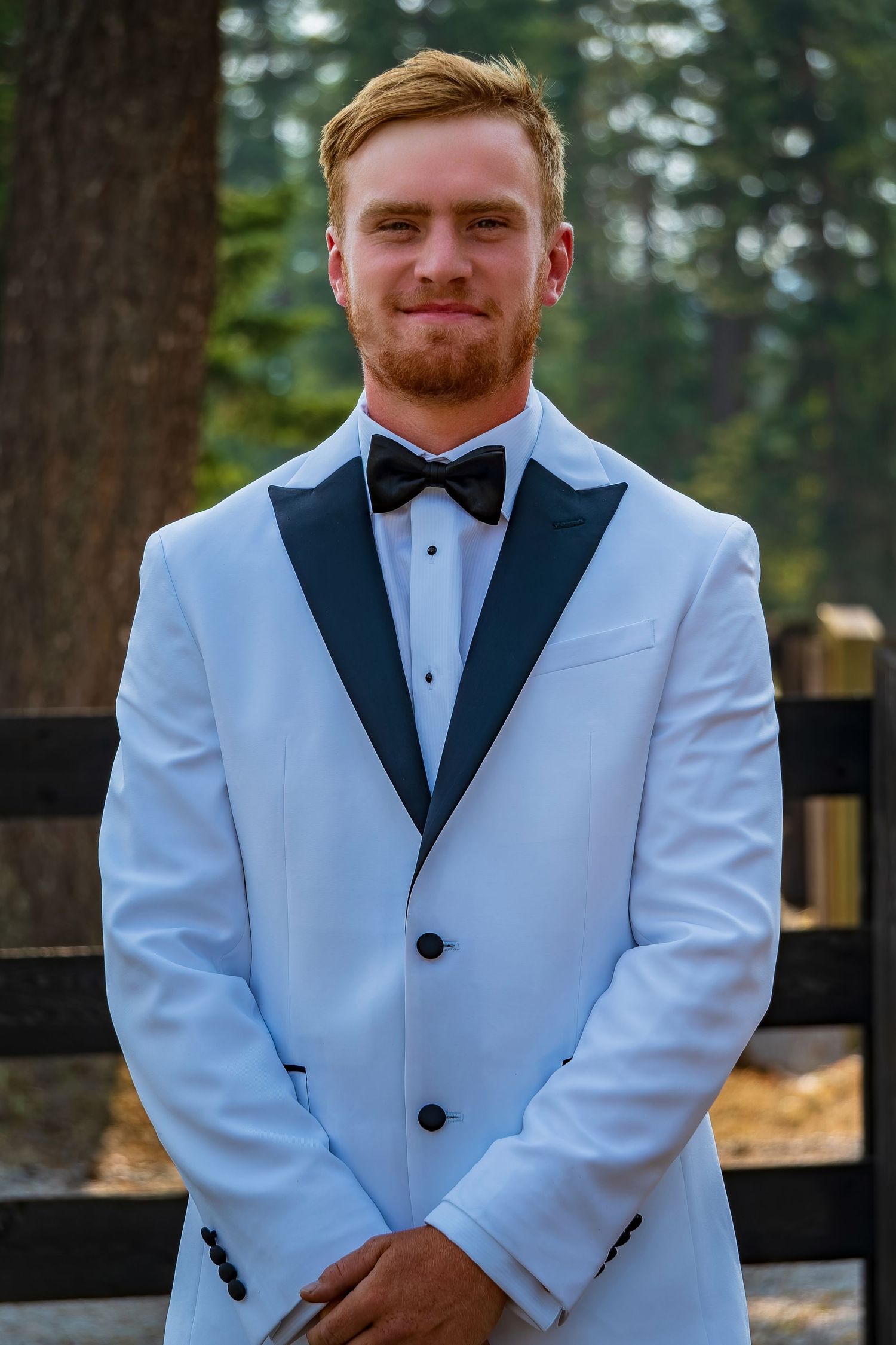 Groom in white tuxedo jacket and black bow tie poses for formal wedding portraits.