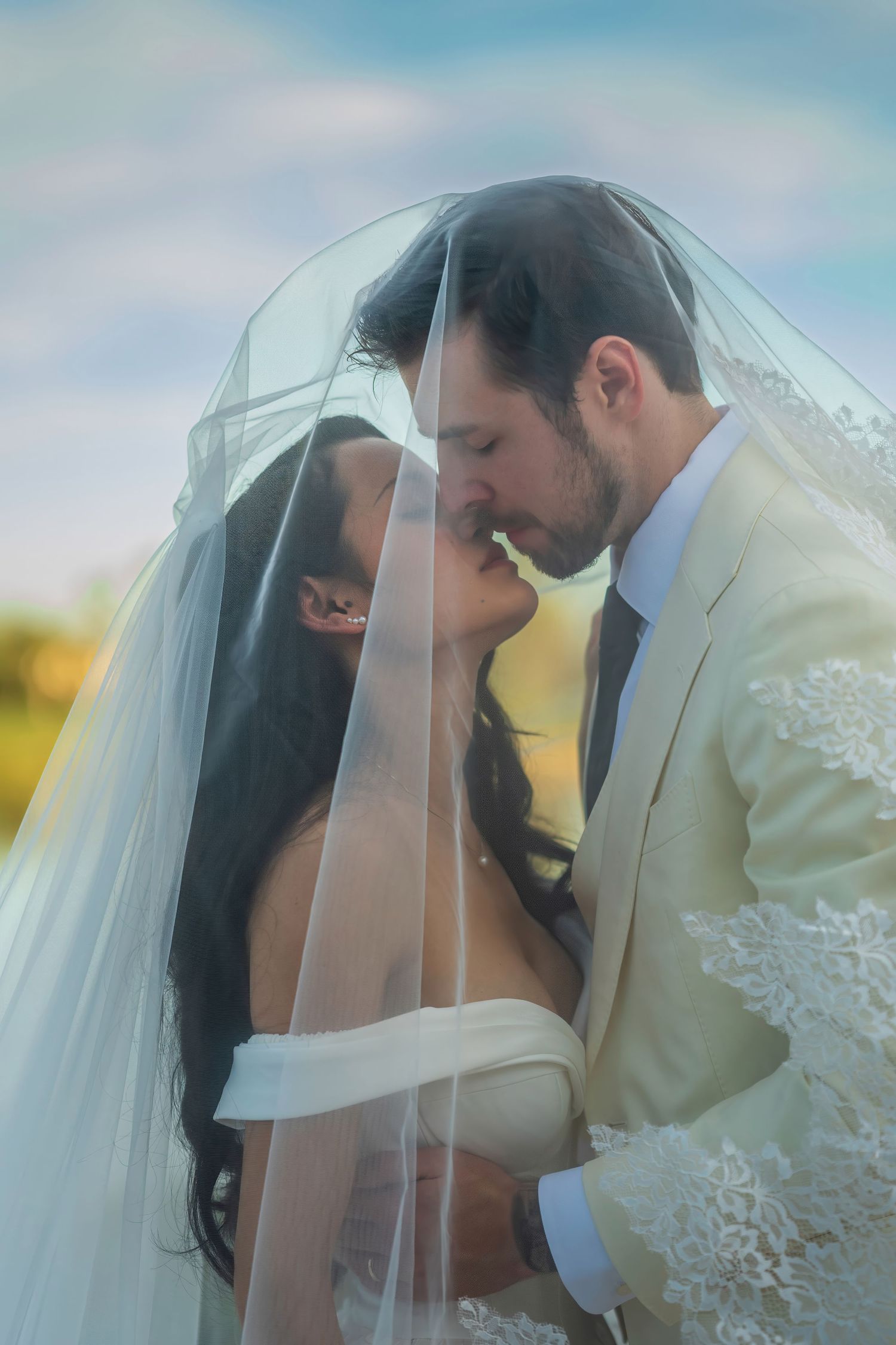 An intimate wedding moment photographed through an elegant white veil with lace details.